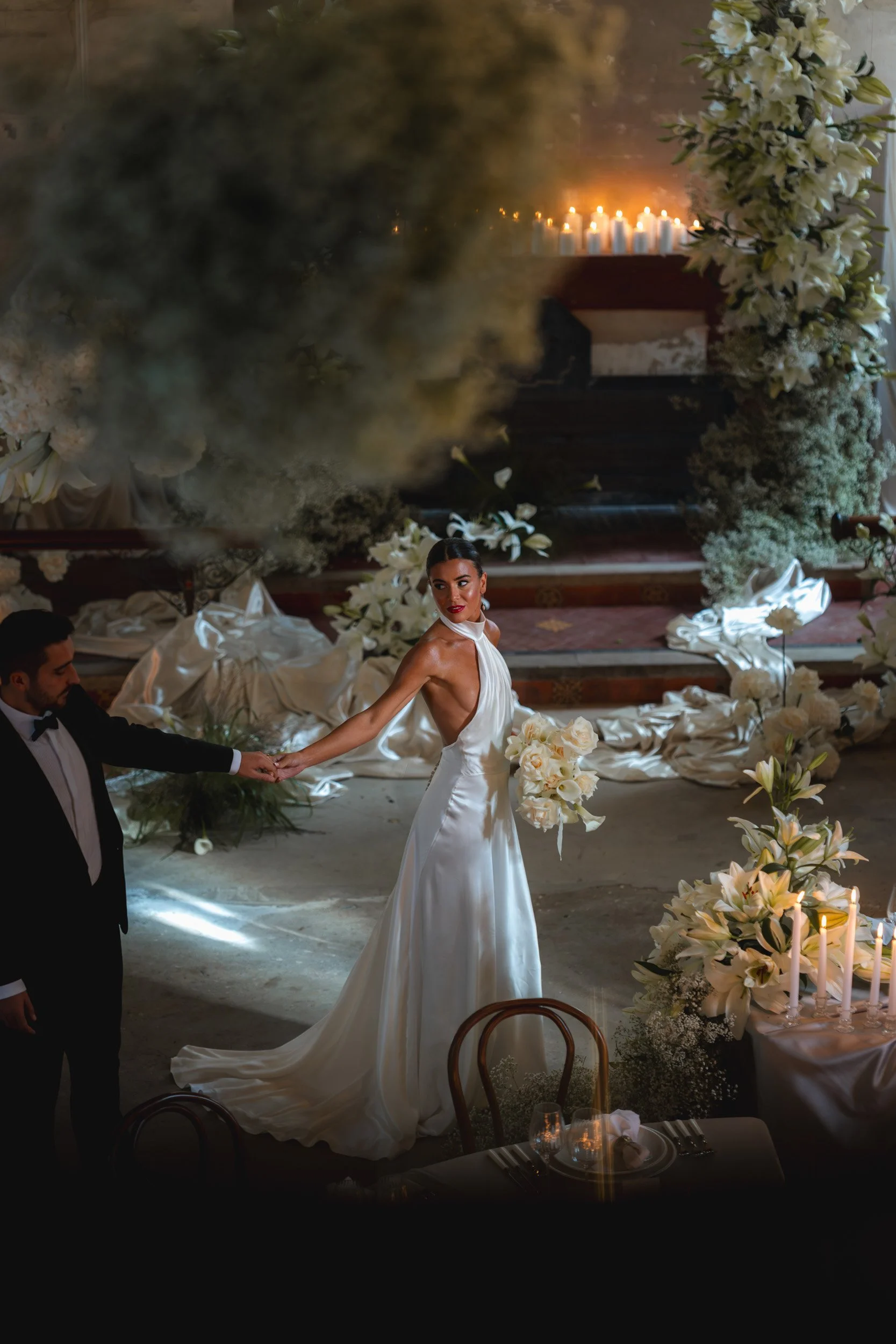 Bride amongst the florals, drapes and candles at a wedding reception in a room with draped fabric inside The Bell Tower at The Elvetham Hotel in Hampshire
