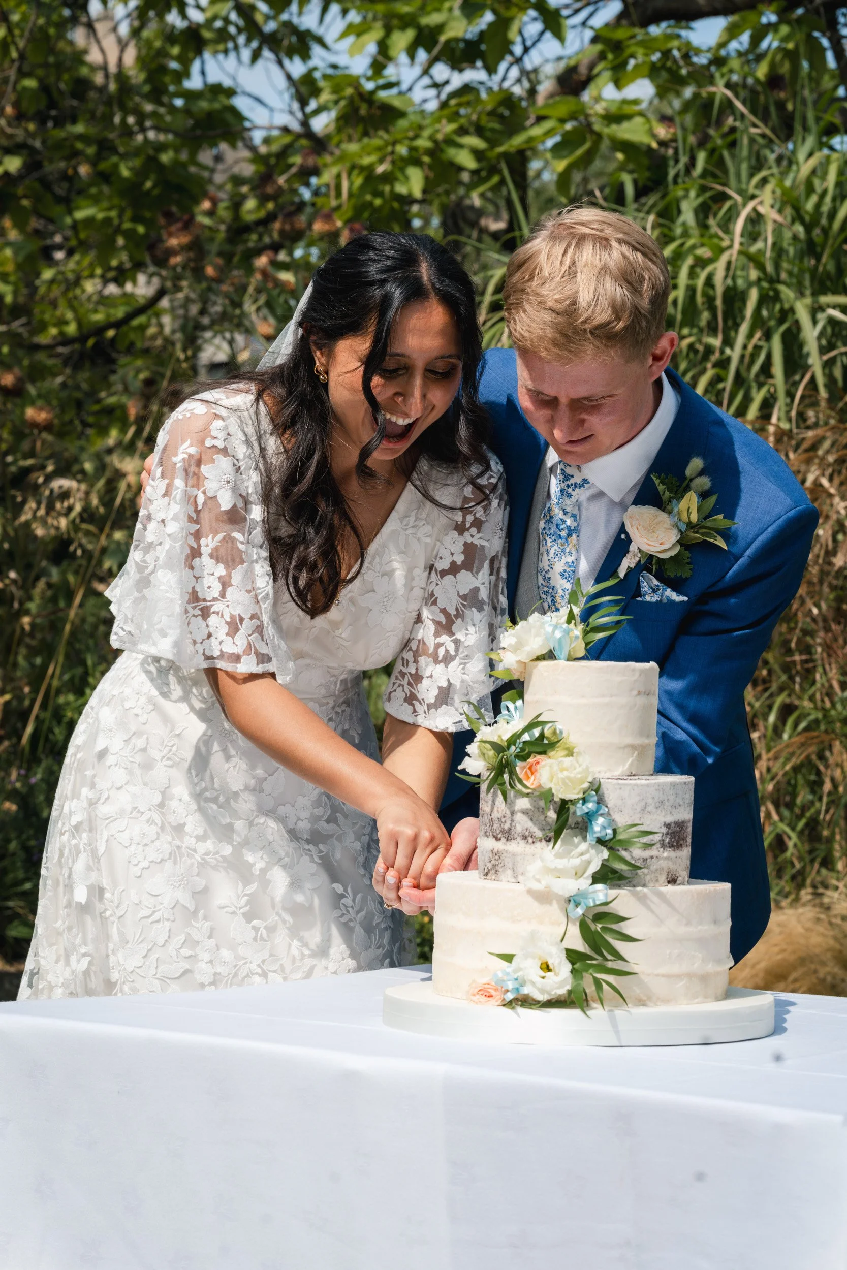 Bride and groom cutting their cake in  the historic gardens of an Oxford University college after the wedding ceremony in Oxford, England
