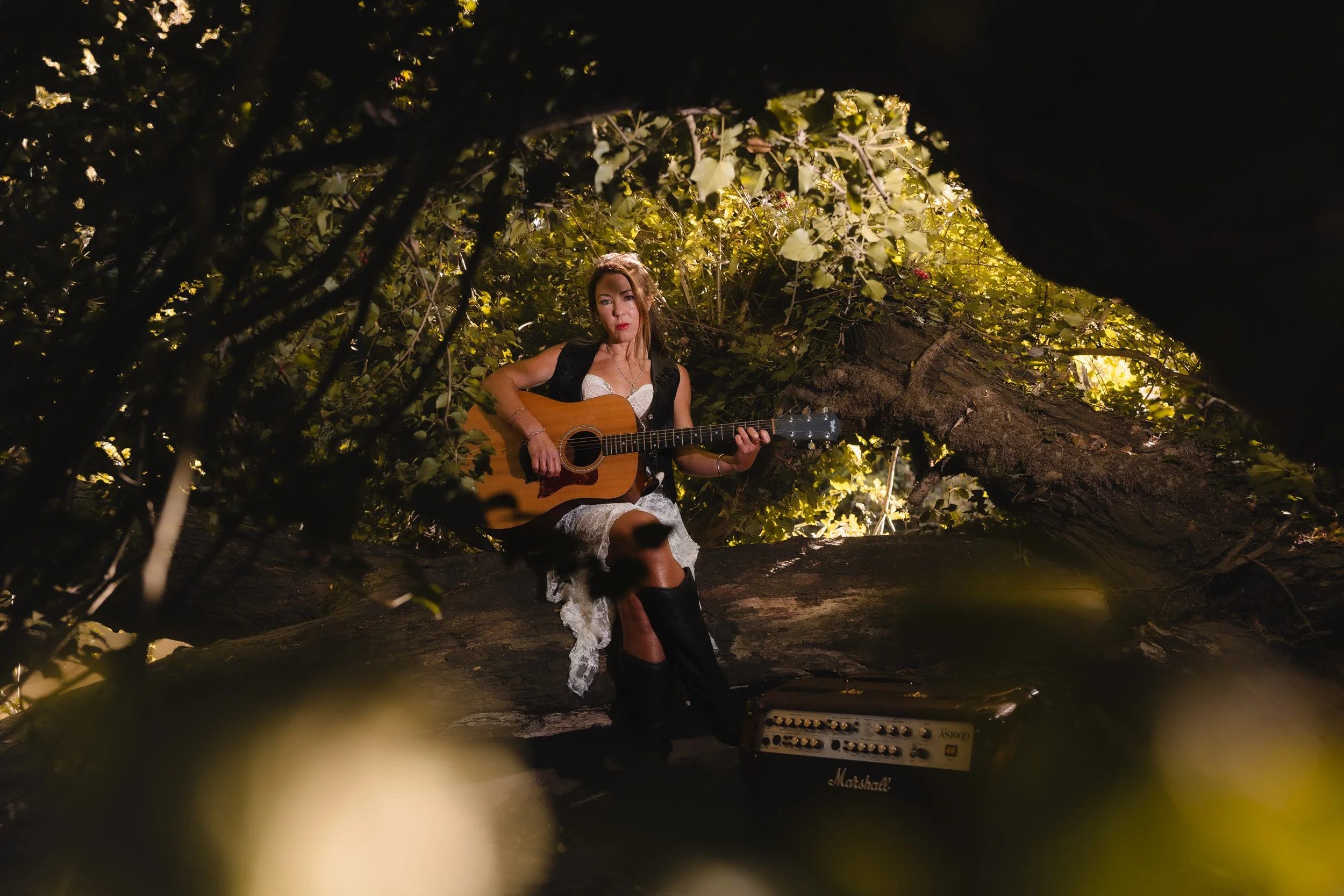 Branding portrait with a musician playing the guitar with her cowboy boots on the amp among the trees the park in Windsor Berkshire
