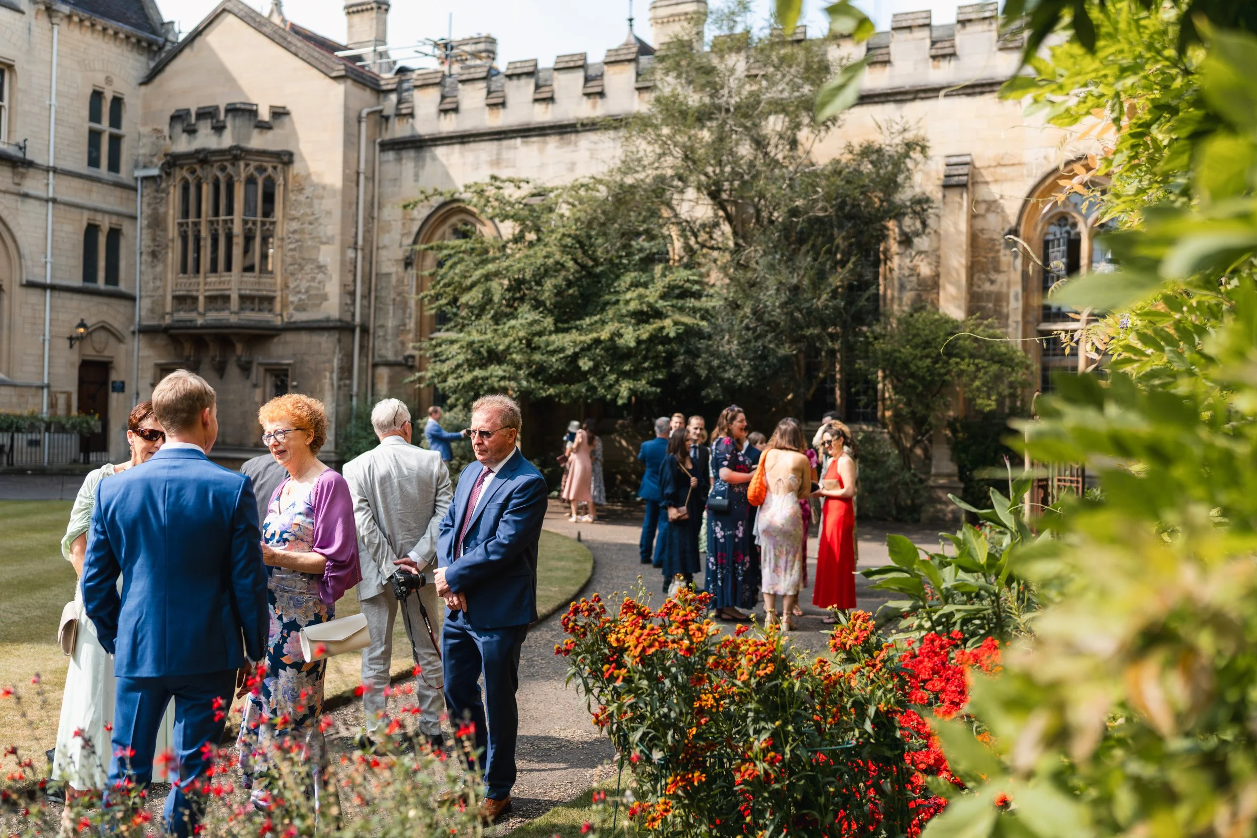 Wedding guests gathering in  the historic gardens of an Oxford University college before the wedding ceremony in Oxford, England