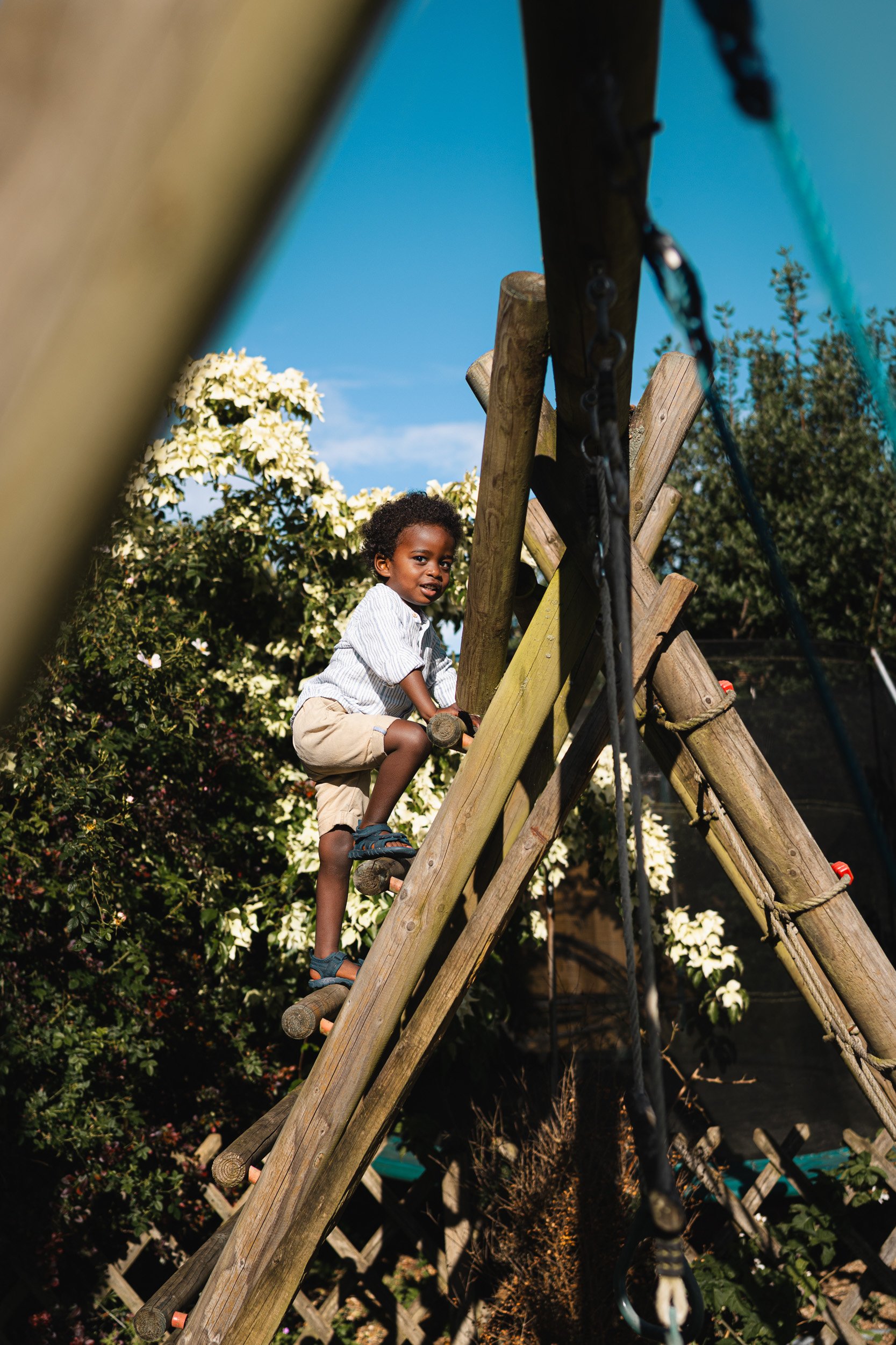 Young child climbing a wooden play frame during a relaxed at-home family photography session in Amersham, Buckinghamshire