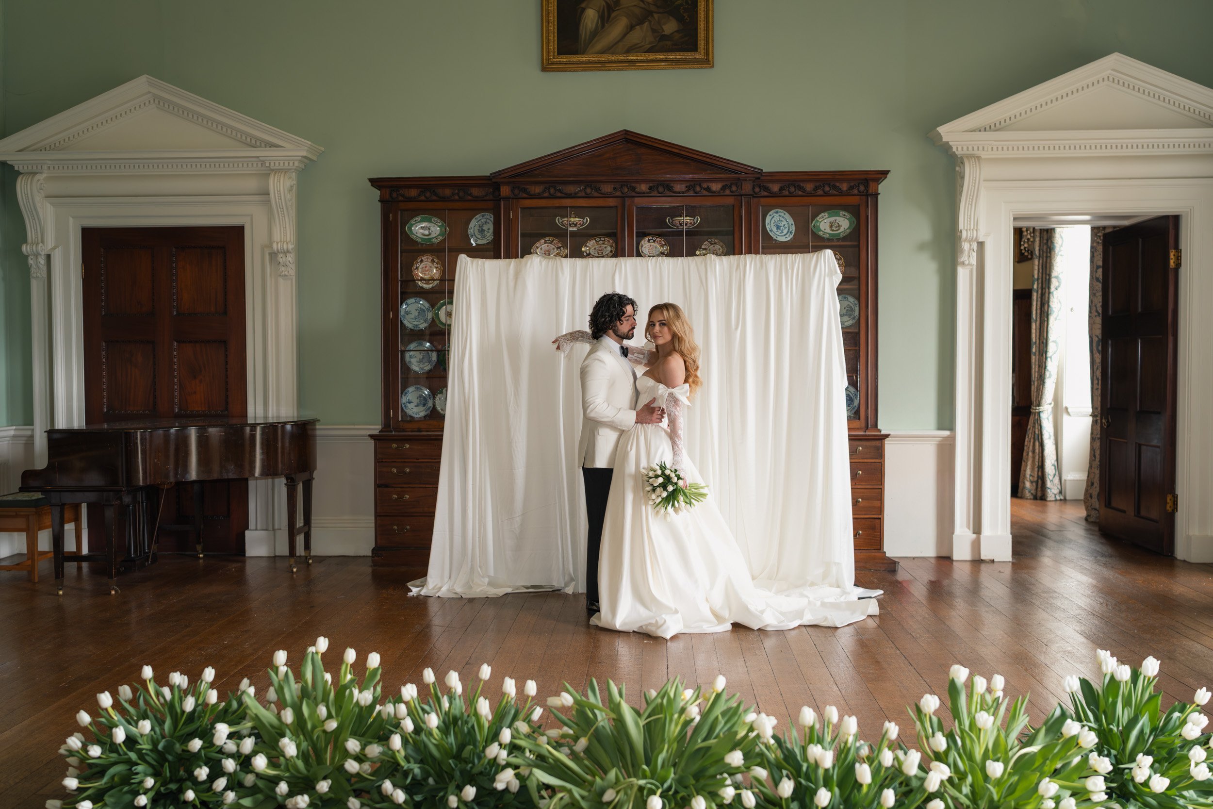 Bride and groom embracing in front of a white backdrop with tulip-lined reception floor at Kirtlington Park in Oxfordshire