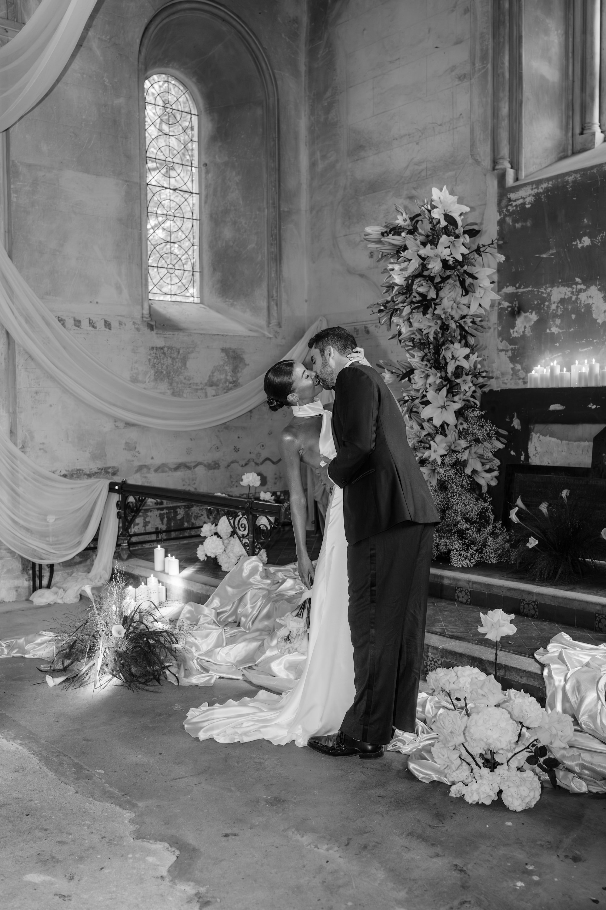 Bride and groom kissing inside The Bell Tower at The Elvetham in Hampshire beneath the arched window and floral arrangement