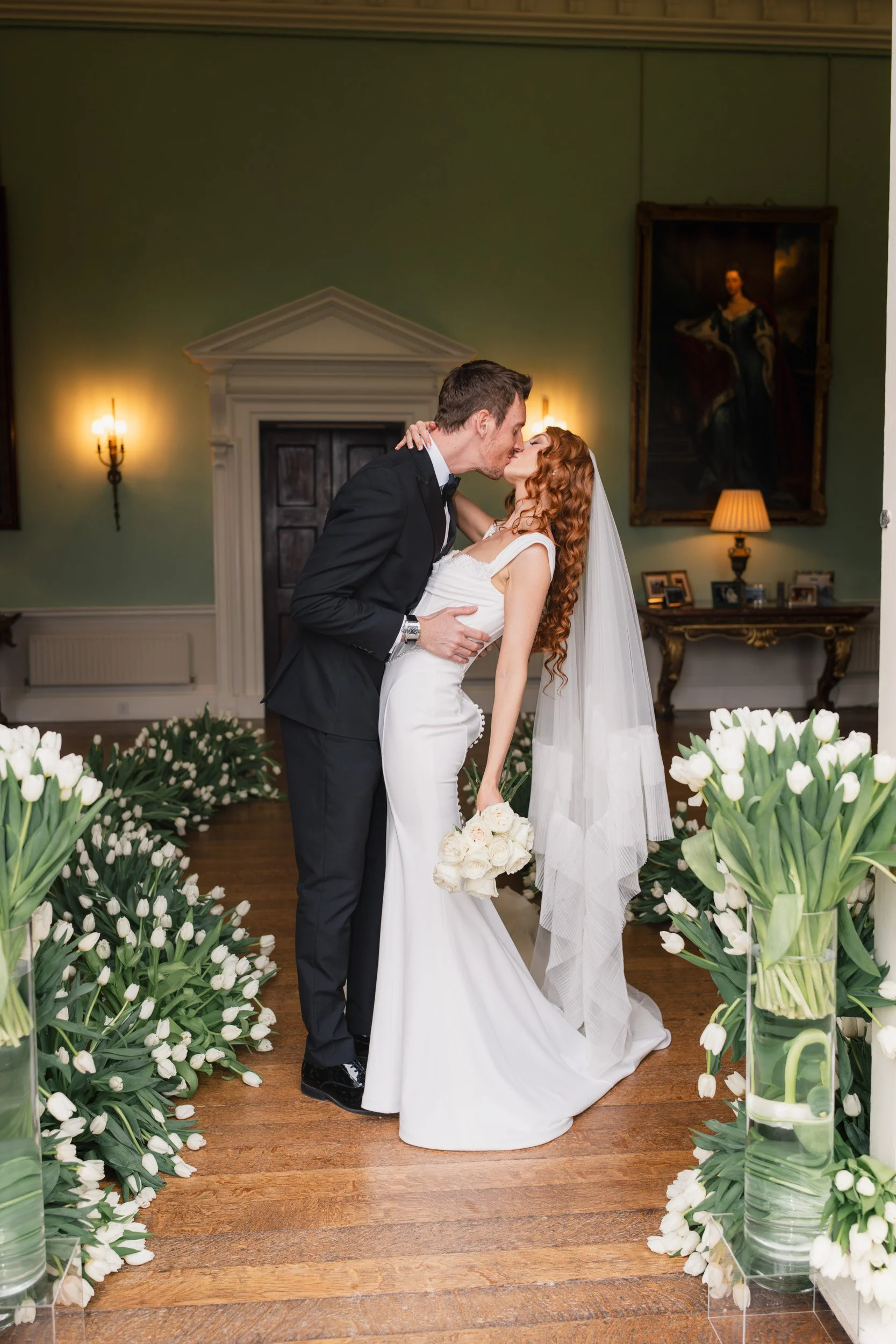 Bride and groom kissing in a tulip-lined aisle during their reception at Kirtlington Park in Oxfordshire
