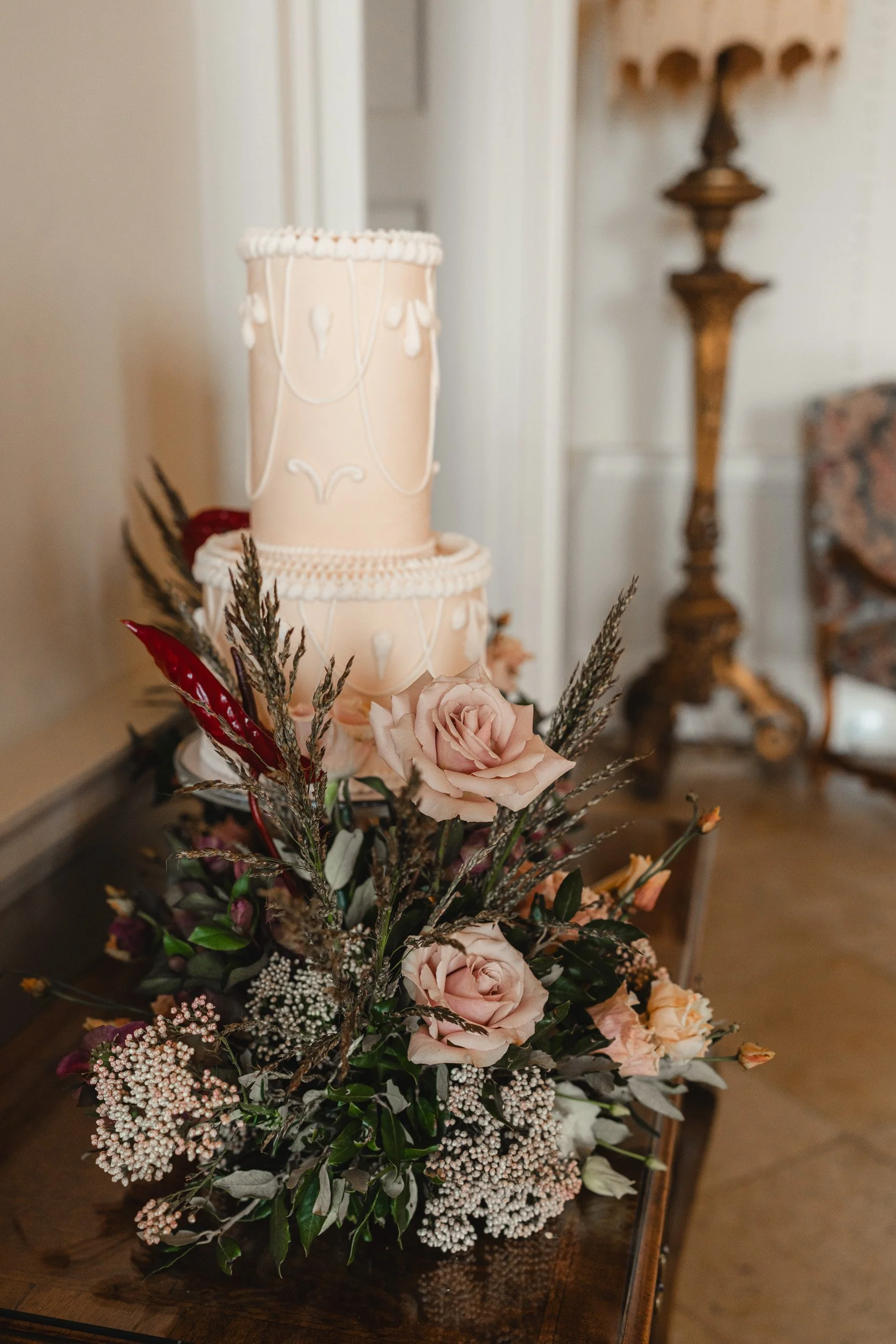 Close-up of a soft pink wedding cake surrounded by matching floral arrangements at Kirtlington Park in Oxfordshire 