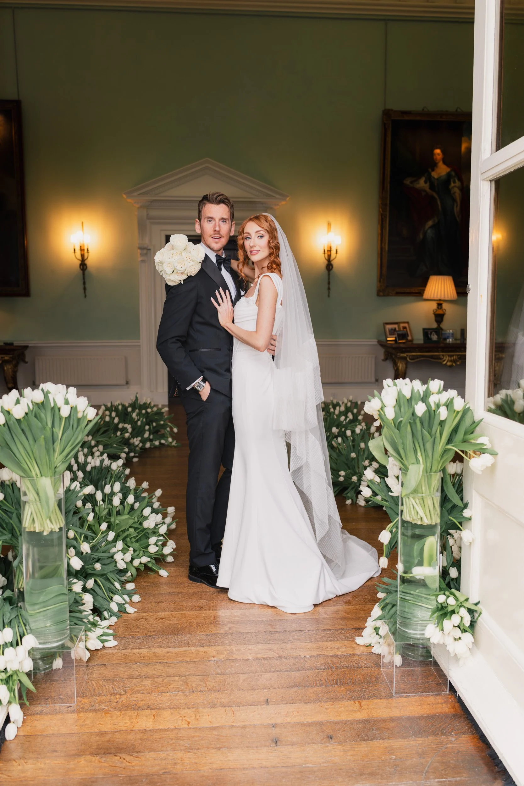 Bride and groom standing in a tulip-lined aisle during their reception at Kirtlington Park in Oxfordshire