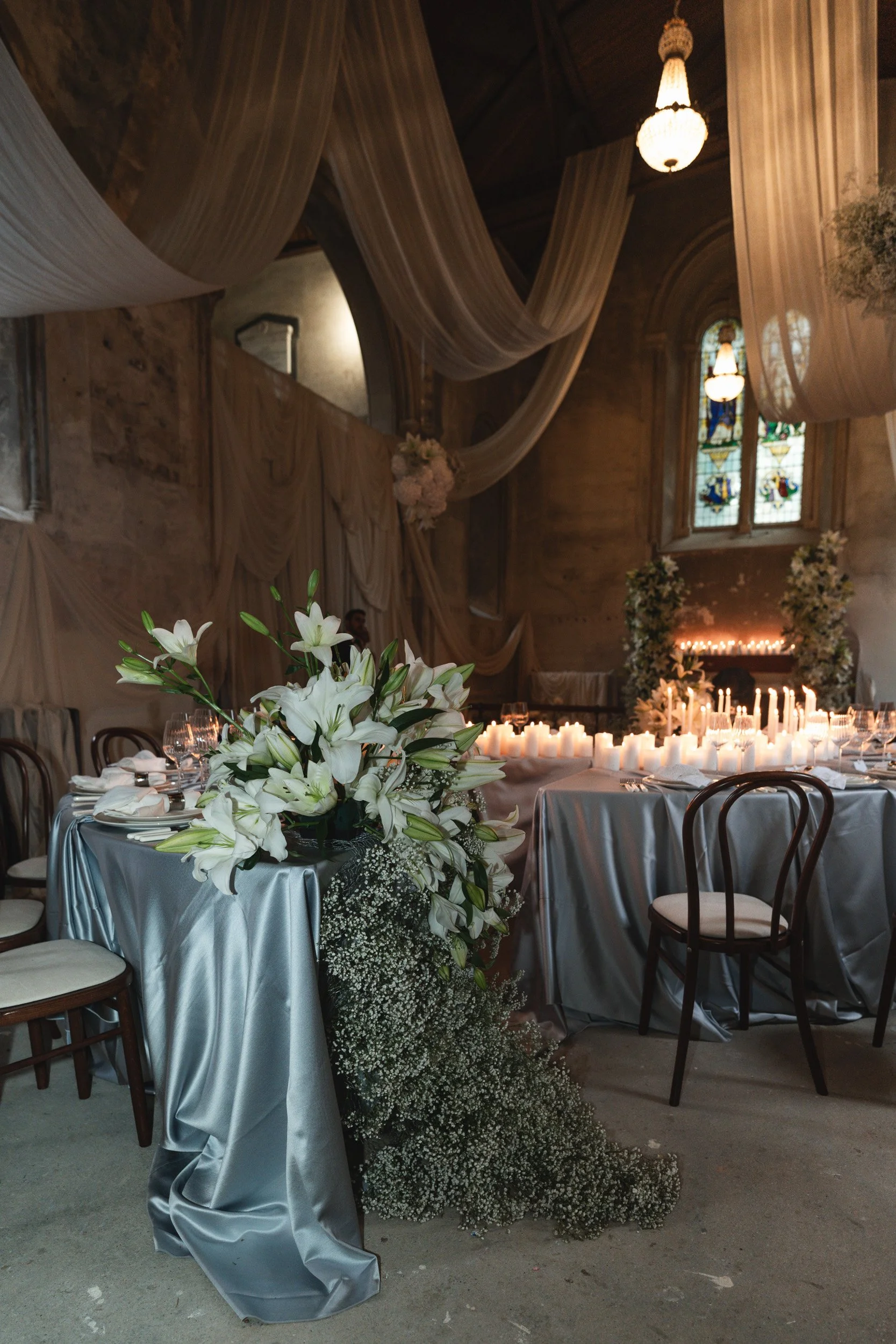 The head table in of a candlelit wedding reception in a  room with draped fabric and floral displays inside The Bell Tower at The Elvetham Hotel in Hampshire