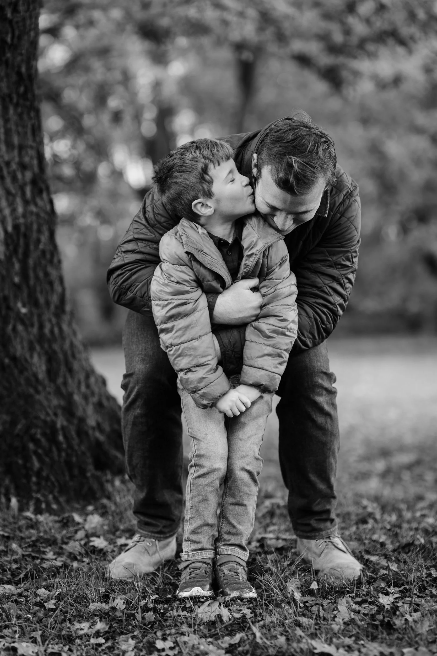A father and his young son having a cuddle under an oak tree during a family photography session in Amersham, Buckinghamshire