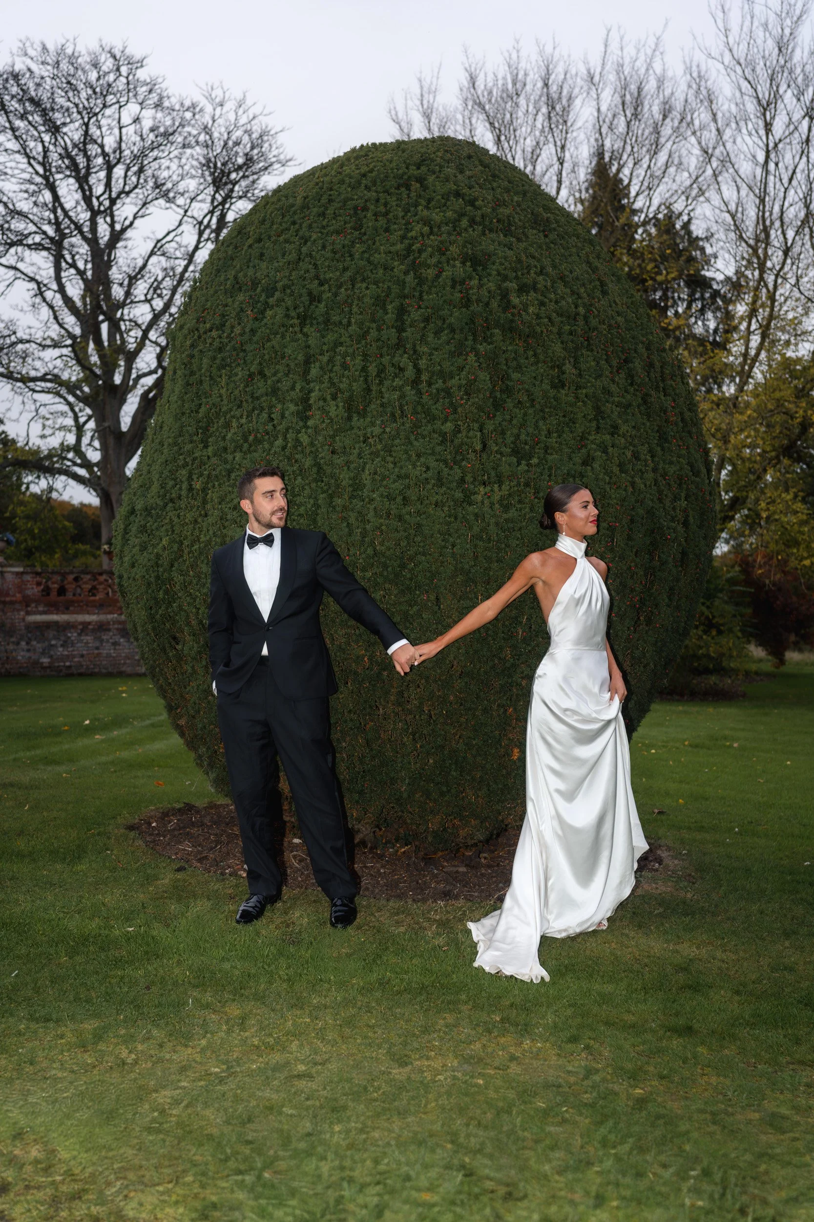 Bride and groom hiding from each other outside  in the gardens of The Elvetham Hotel in Hampshire 
