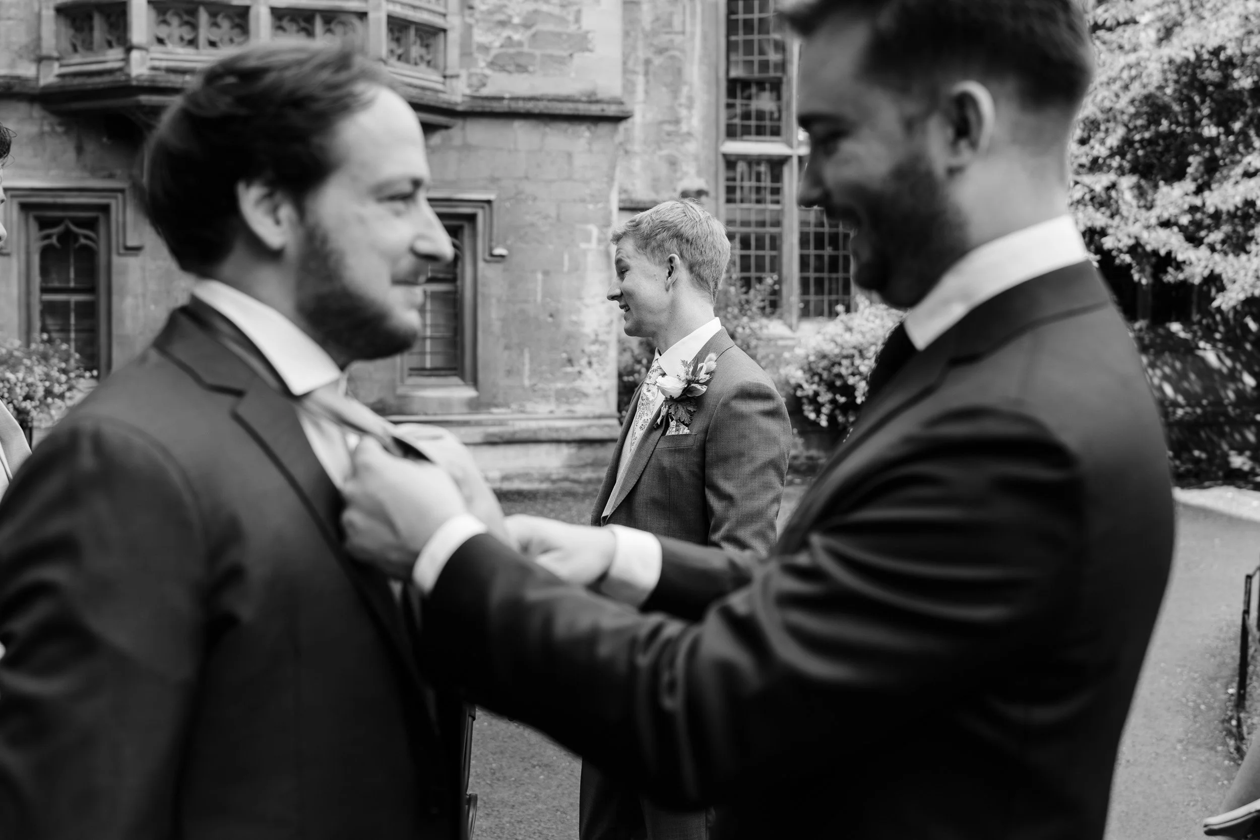 Groomsmen adjusting the grooms tie in the gardens Oxford University college before the wedding ceremony in Oxford, England