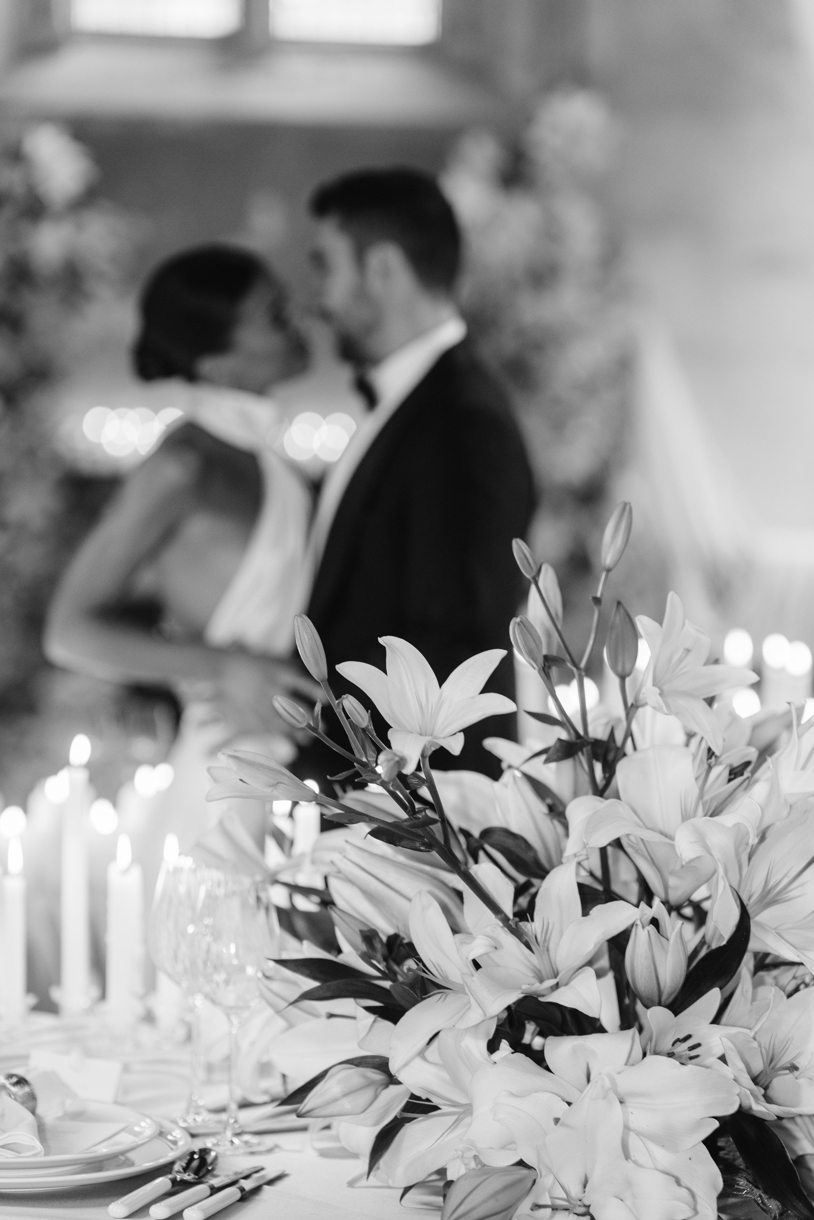 Bride and groom kissing at their reception at The Bell Tower at The Elvetham Hotel in Hampshire with soft focus on the newly weds and details in the florals and candles