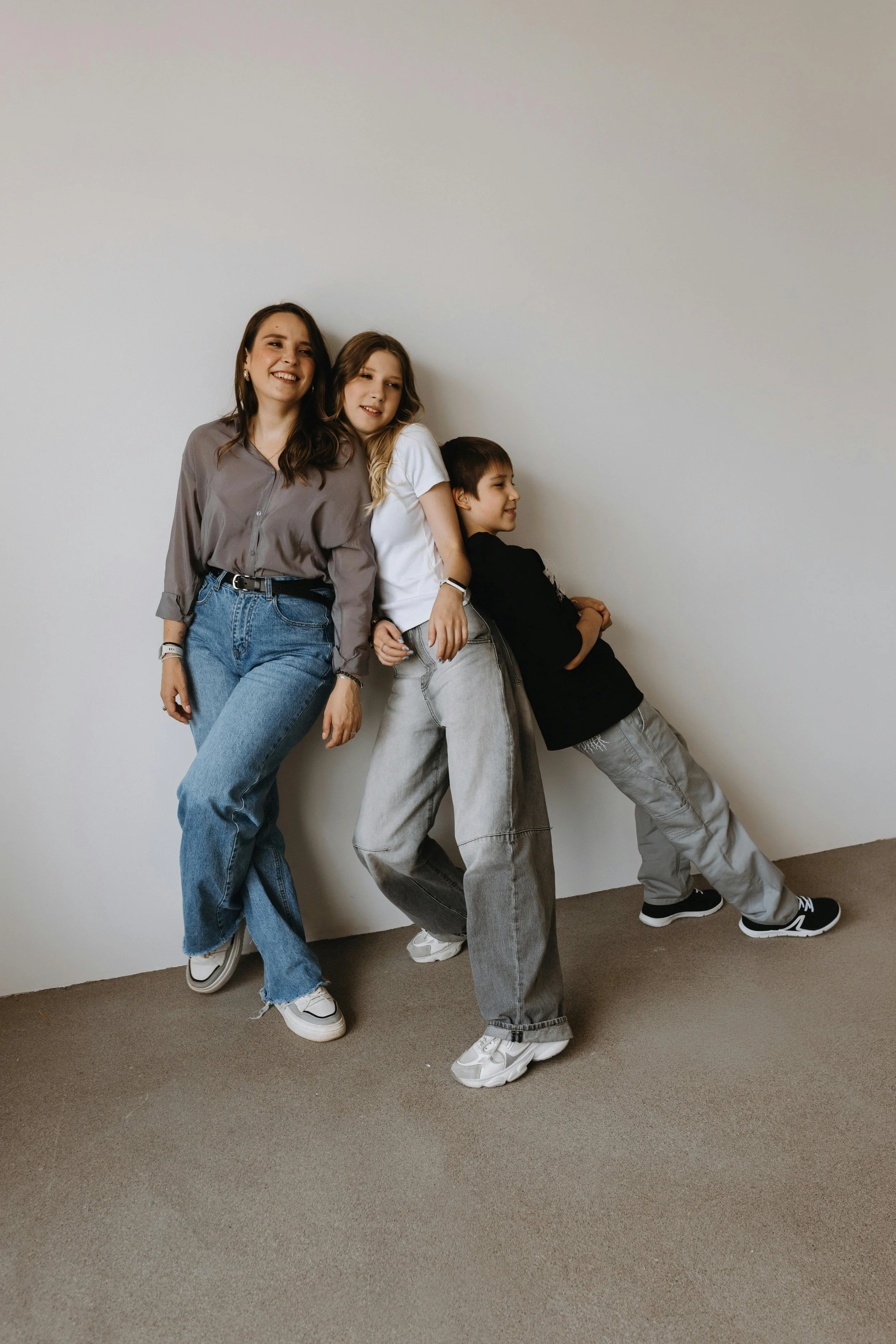Three children standing against a plain wall, smiling and posing.