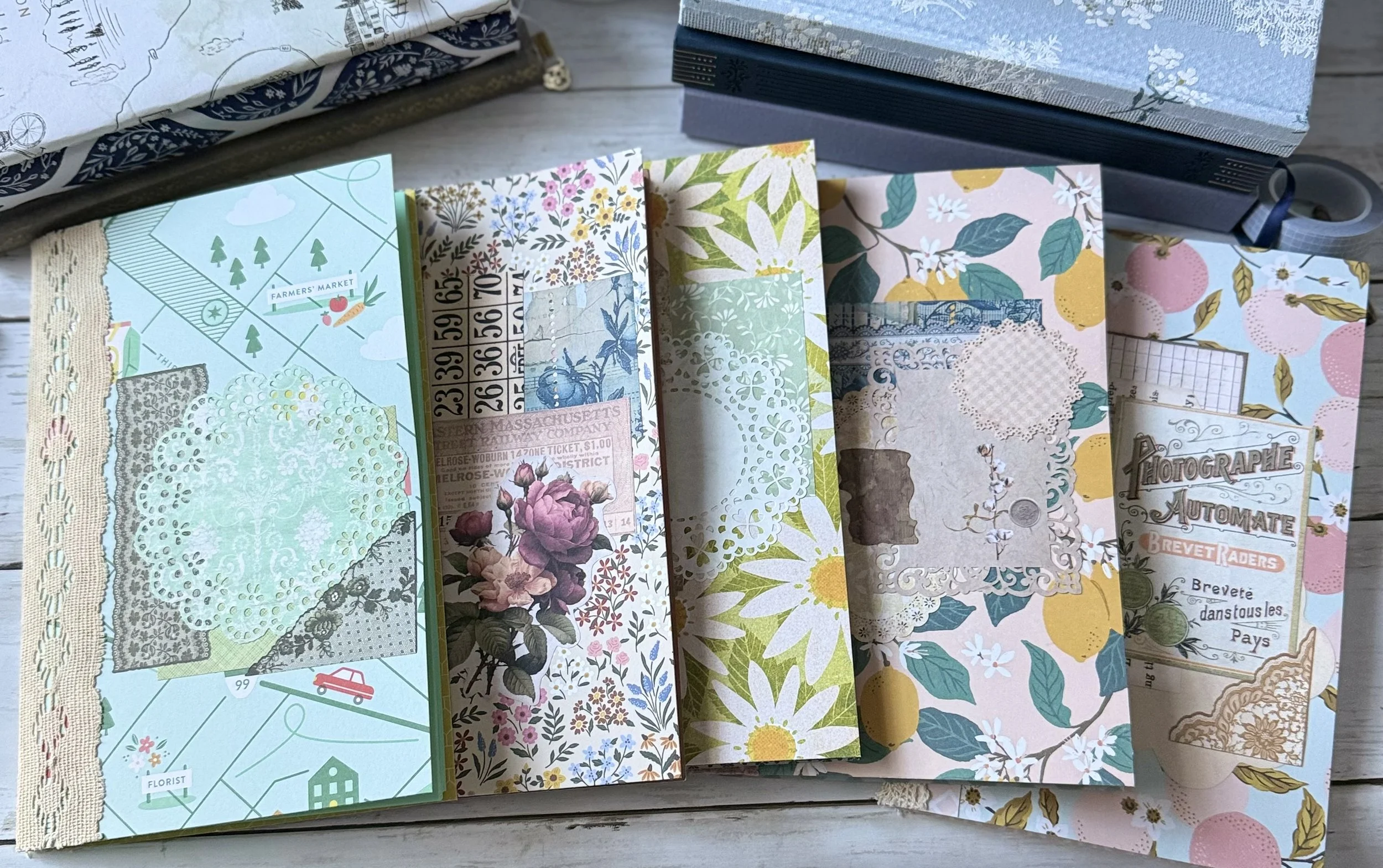 Overhead view of vintage floral journals, patterned papers, lace doilies, and decorative ephemera arranged on a wooden table