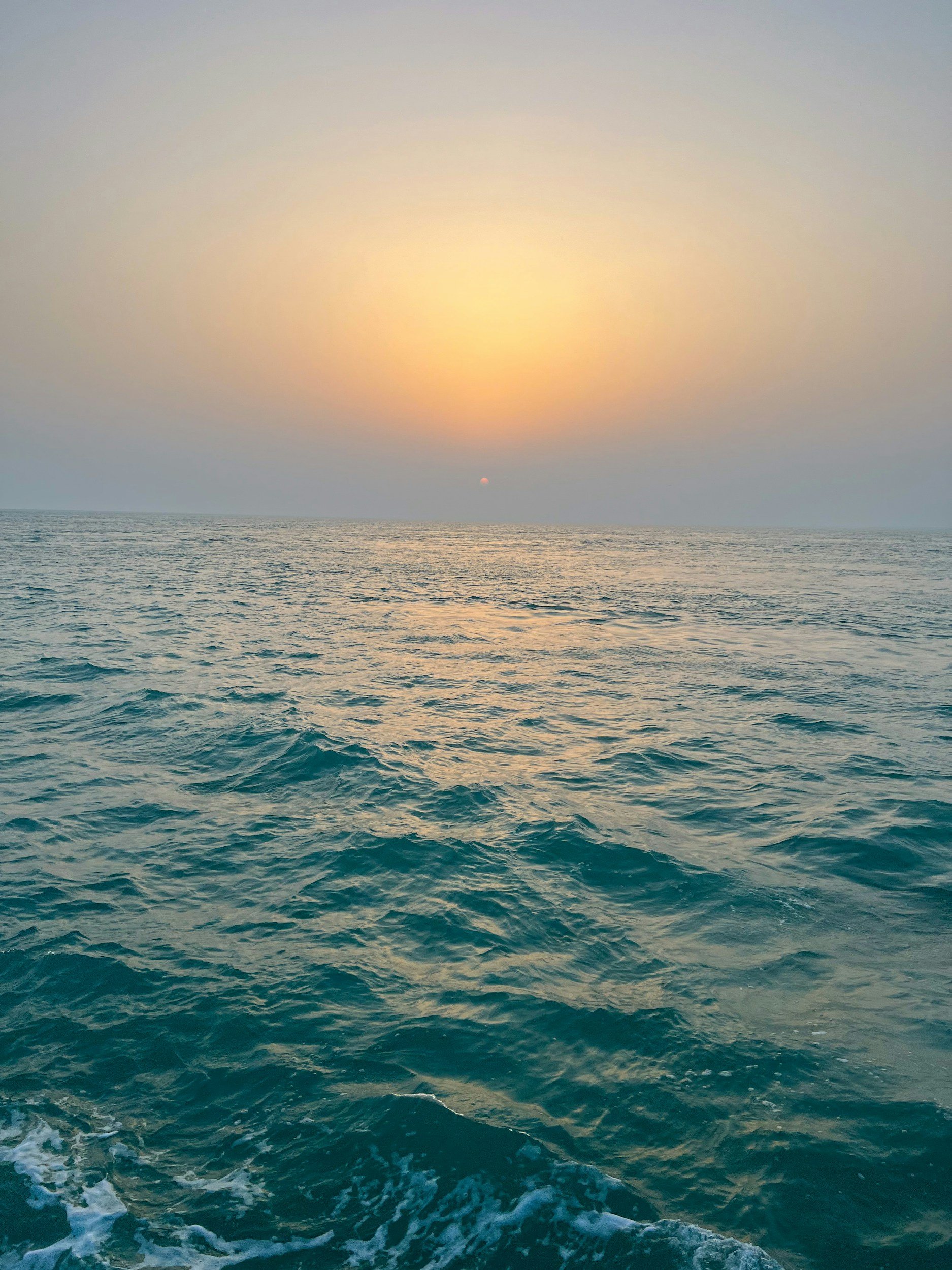 Sunset over the ocean with calm waves and a colorful sky.