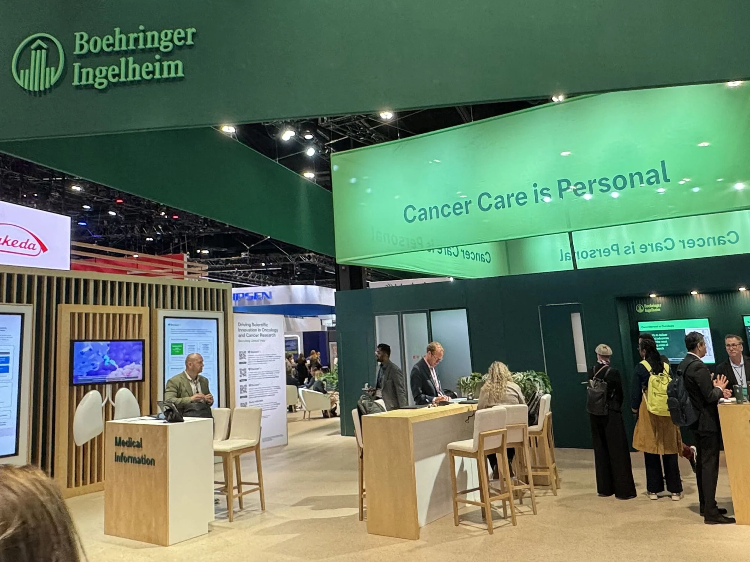Boehringer Ingelheim exhibit at a conference with a green sign reading 'Cancer Care is Personal' and a reception area with people talking and informational displays.
