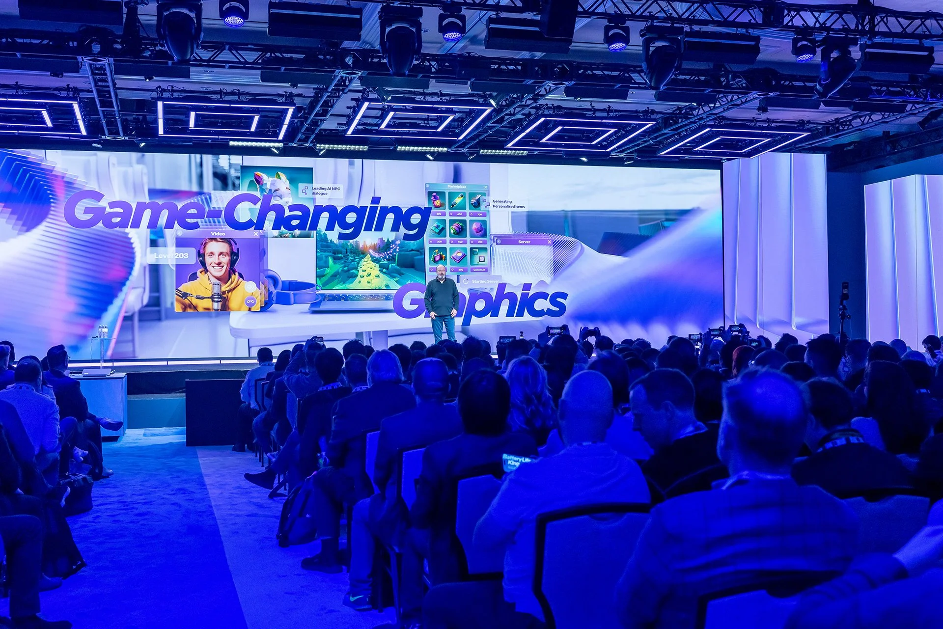 A speaker on stage at a conference presenting about game-changing graphics technology, with a large audience seated in front and blue lighting.