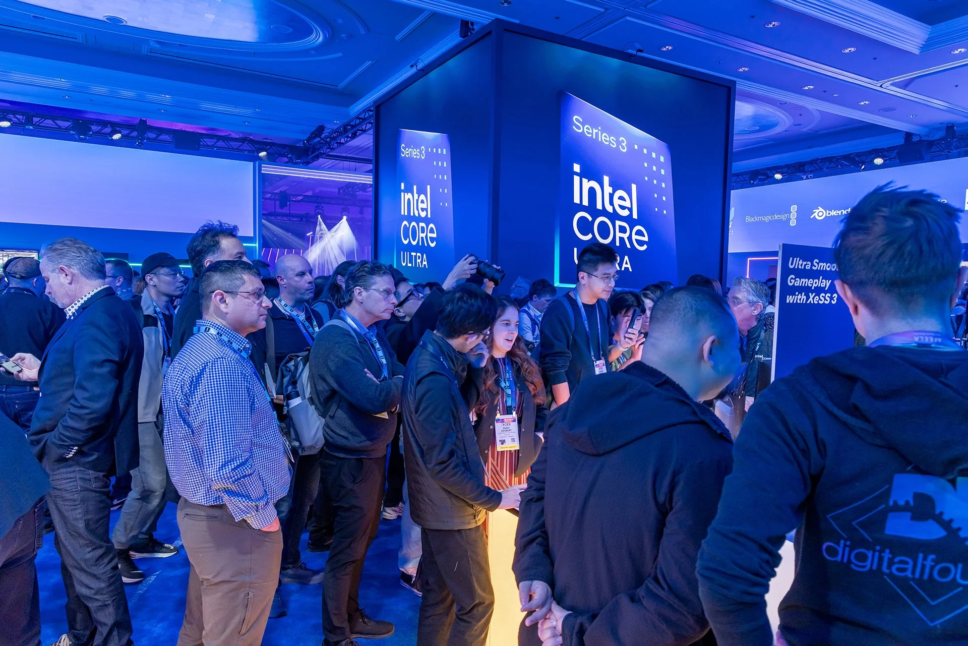 Crowd of people at a technology expo, with large banners displaying Intel Core Ultra branding and several standing monitors.