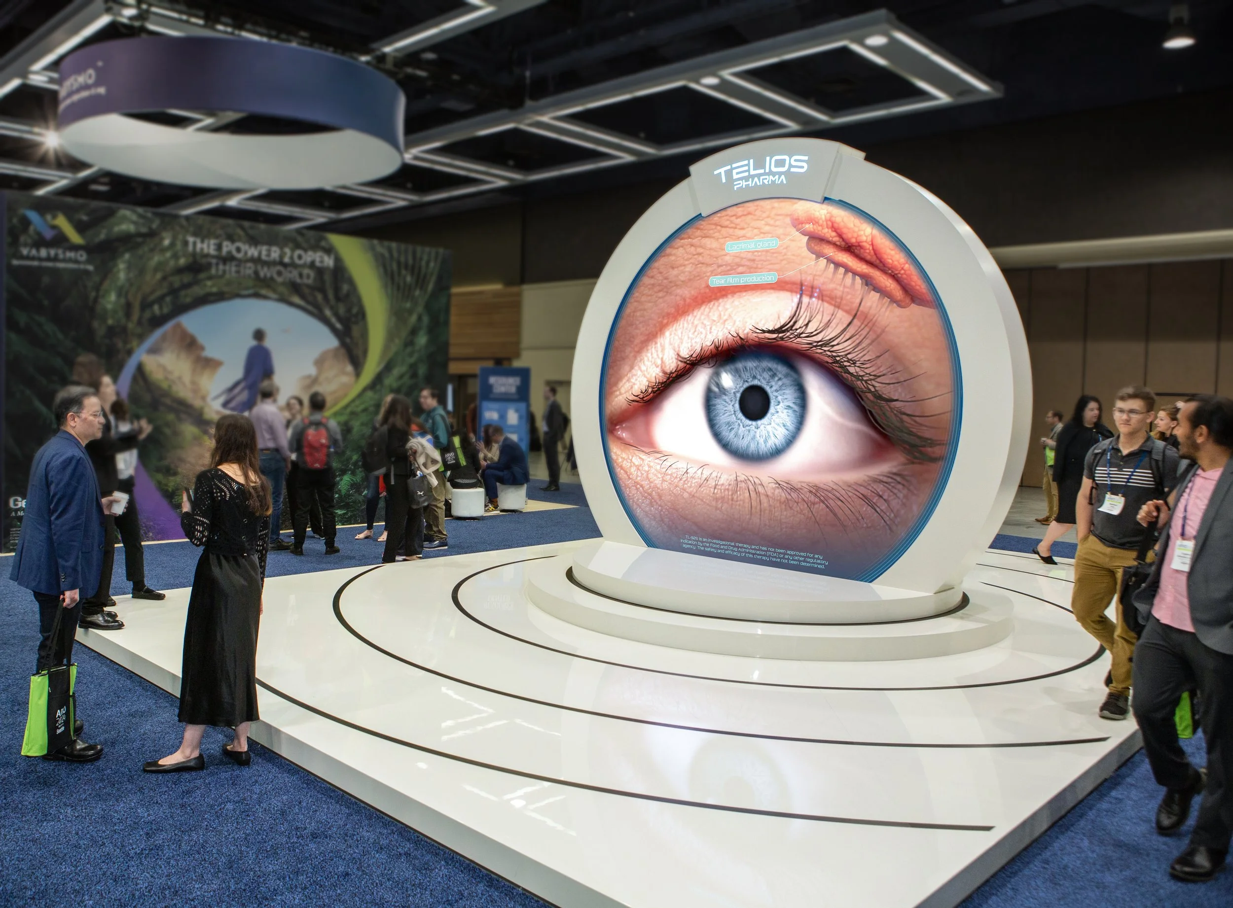 Large exhibition display featuring an oversized eye with labels for the tear film and lacrimal gland. People are walking around and engaging with the exhibits at a conference or trade show.