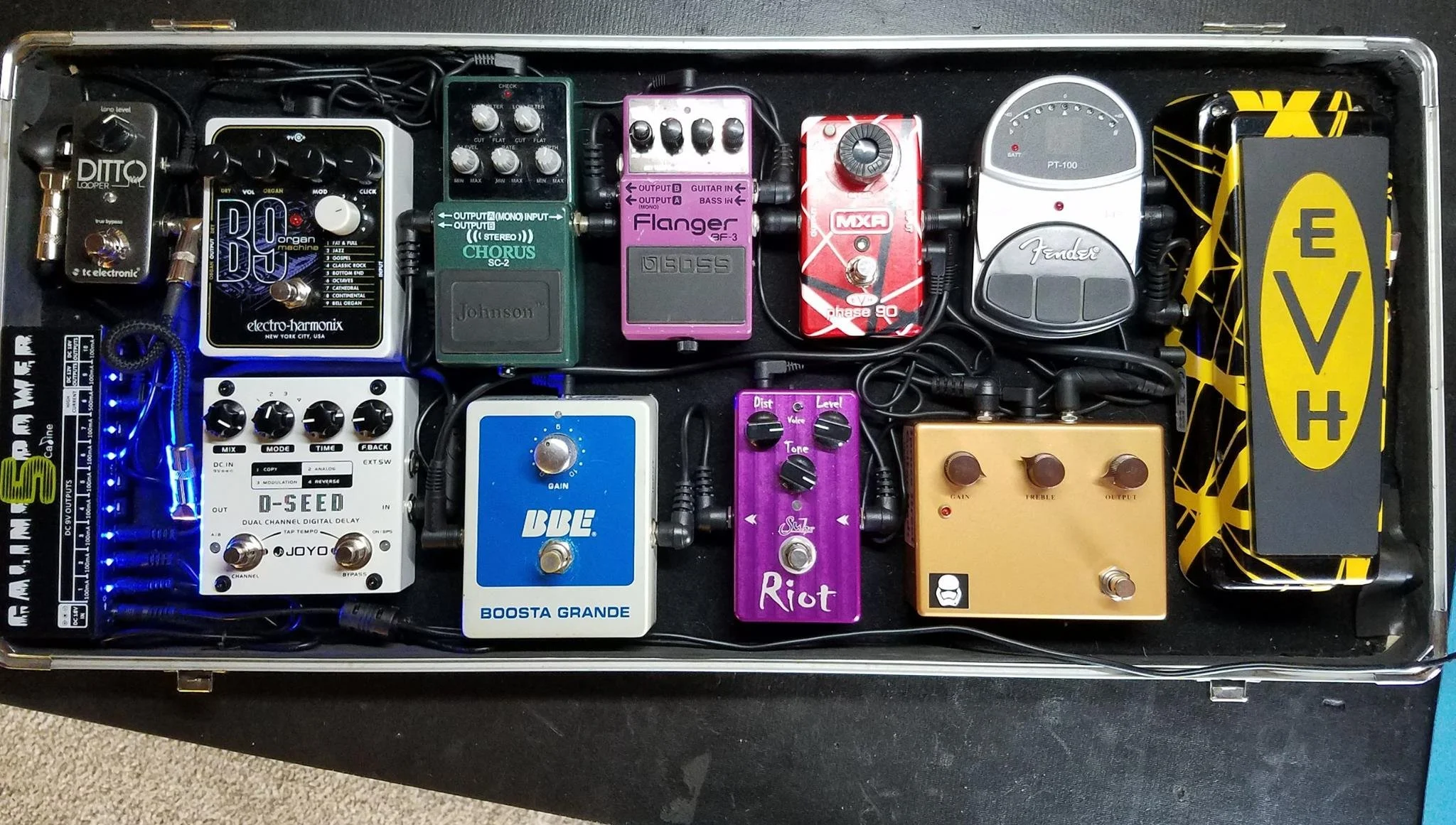 A guitar effects pedalboard with various pedals including a tuner, overdrive, delay, chorus, and distortion, connected by cables, on a black surface.