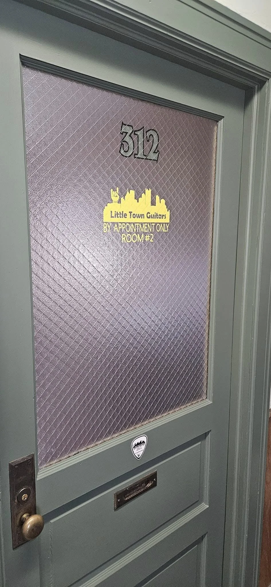 A gray door with textured glass, house number 312, and a yellow sign for Little Town Guitars indicating an appointment-only room.