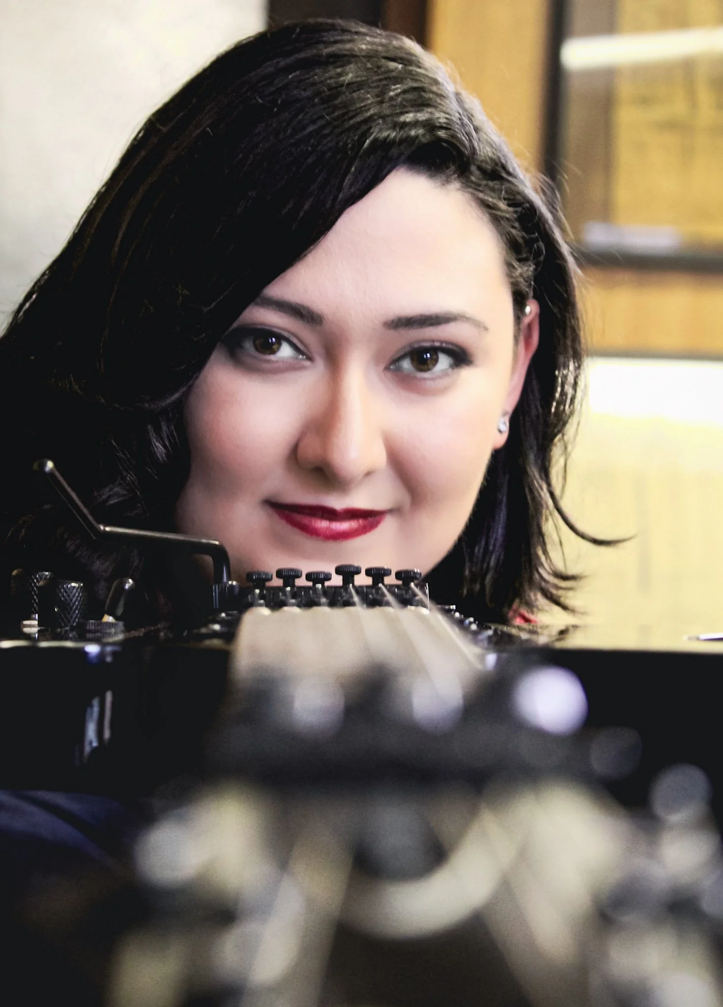 Close-up of a woman with black hair and red lipstick, smiling, with a blurred piano in the foreground.
