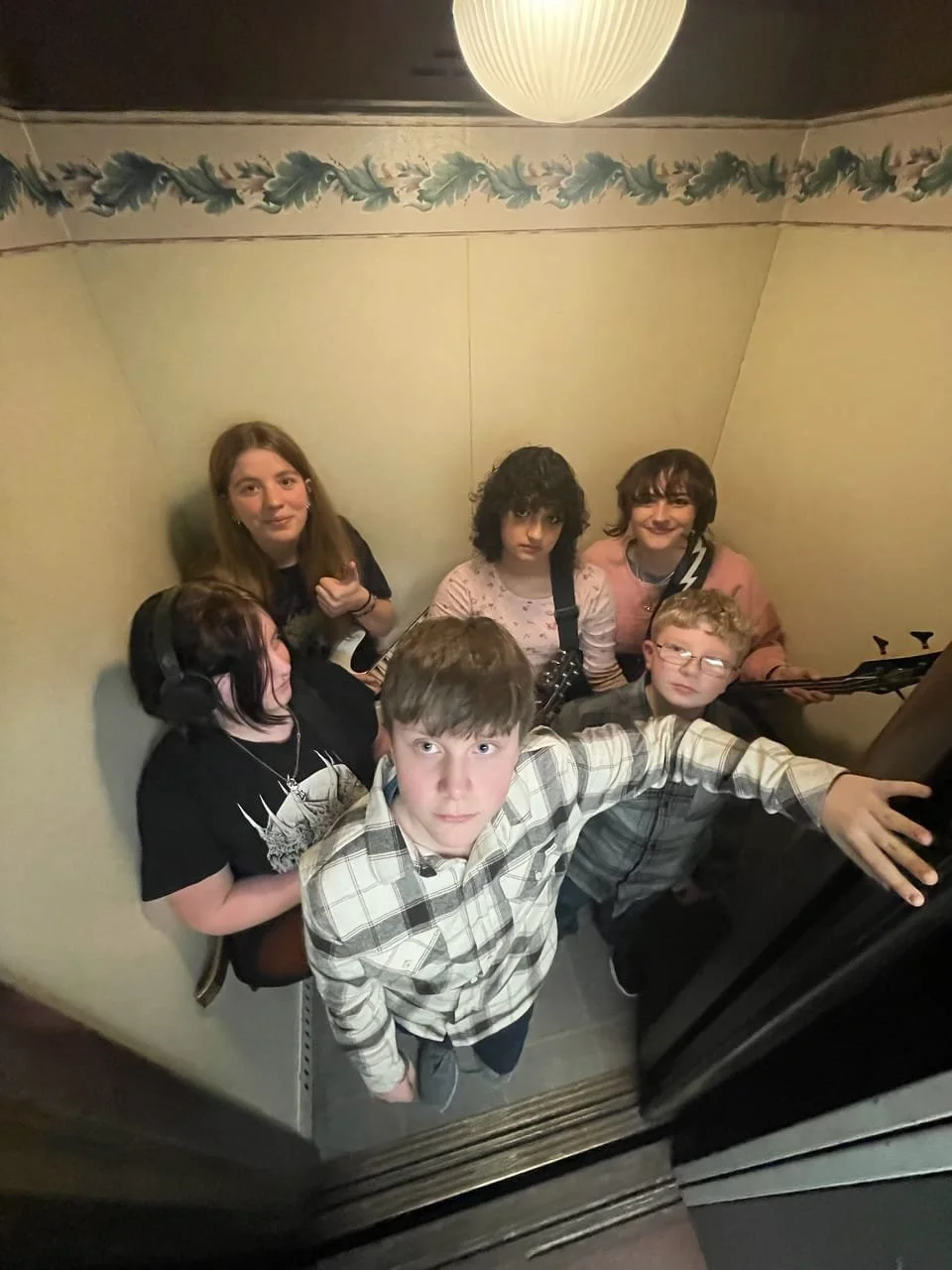 Six children in an elevator, with one kid reaching out and looking at the camera.