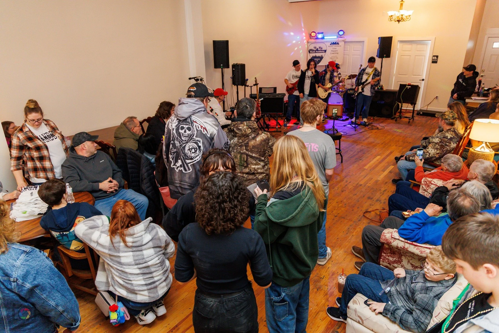 People gathered in a living room watching a live band performance on stage.