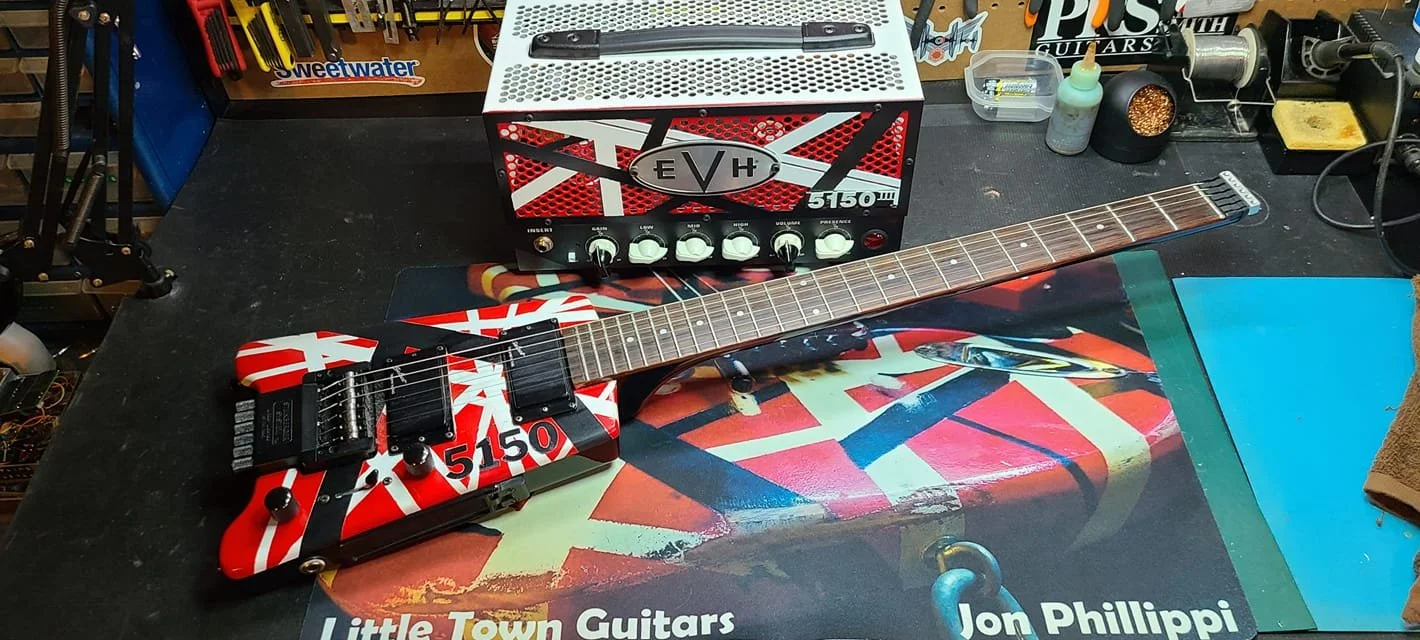 Electric guitar with a red and white striped pattern on its body, placed on a workbench. Behind it, a small amplifier with the label EVH 5150 III.