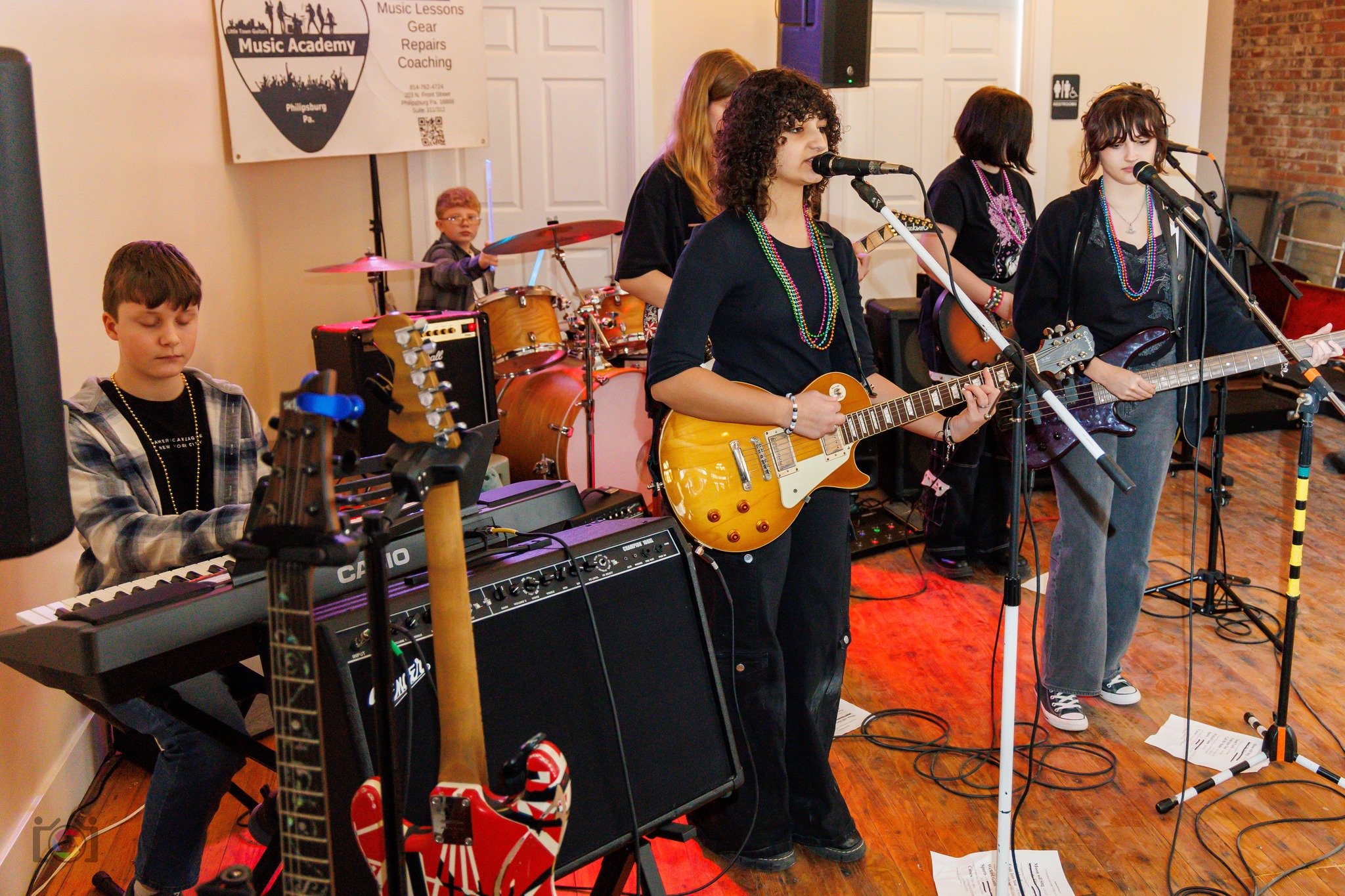 A band of five young musicians performing on stage with instruments including electric guitars, a keyboard, and drums at Music Academy in Phillipsburg, PA.