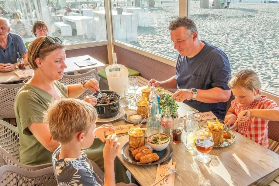 Une famille en vacances mangeant dans un restaurant près de la plage, avec des plats de nourriture sur la table.