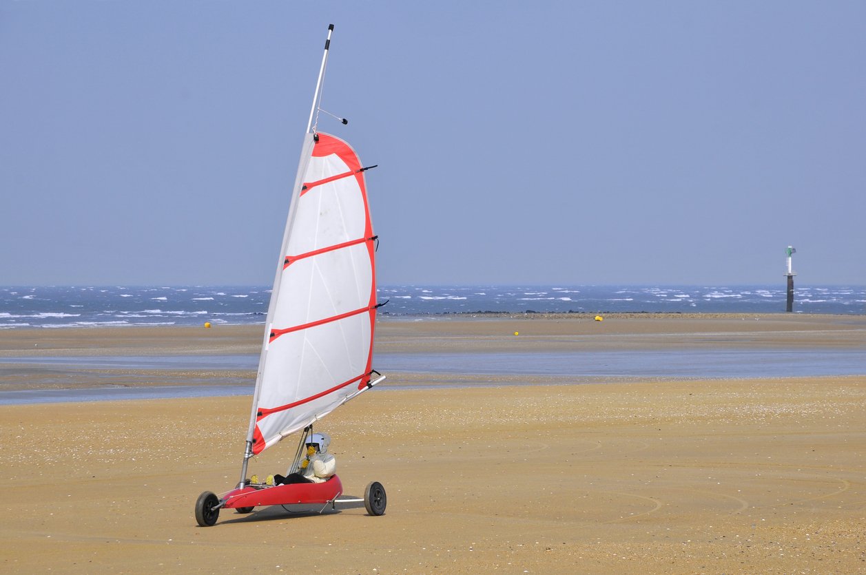 Une voiturette de sport avec une voile de planche à voile sur une plage, avec la mer en arrière-plan.