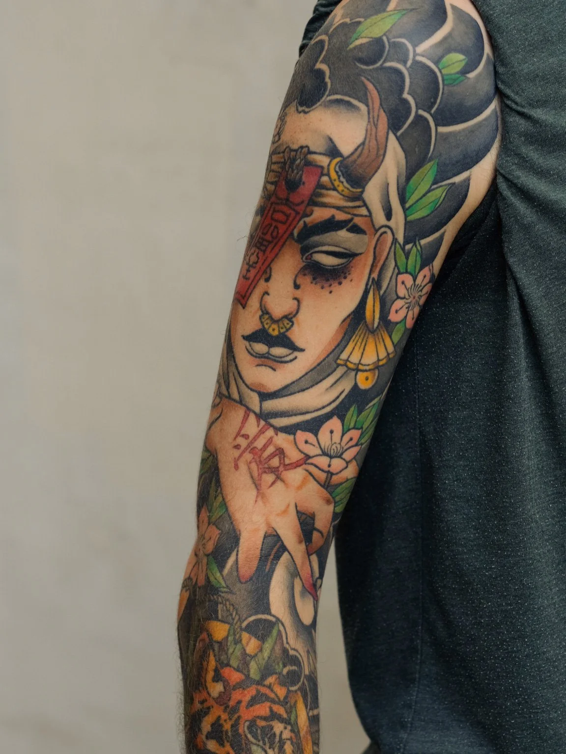 Tattoo på en persons arm, der viser en kvindelig afbildning med blomster, fjær, og skrifter.