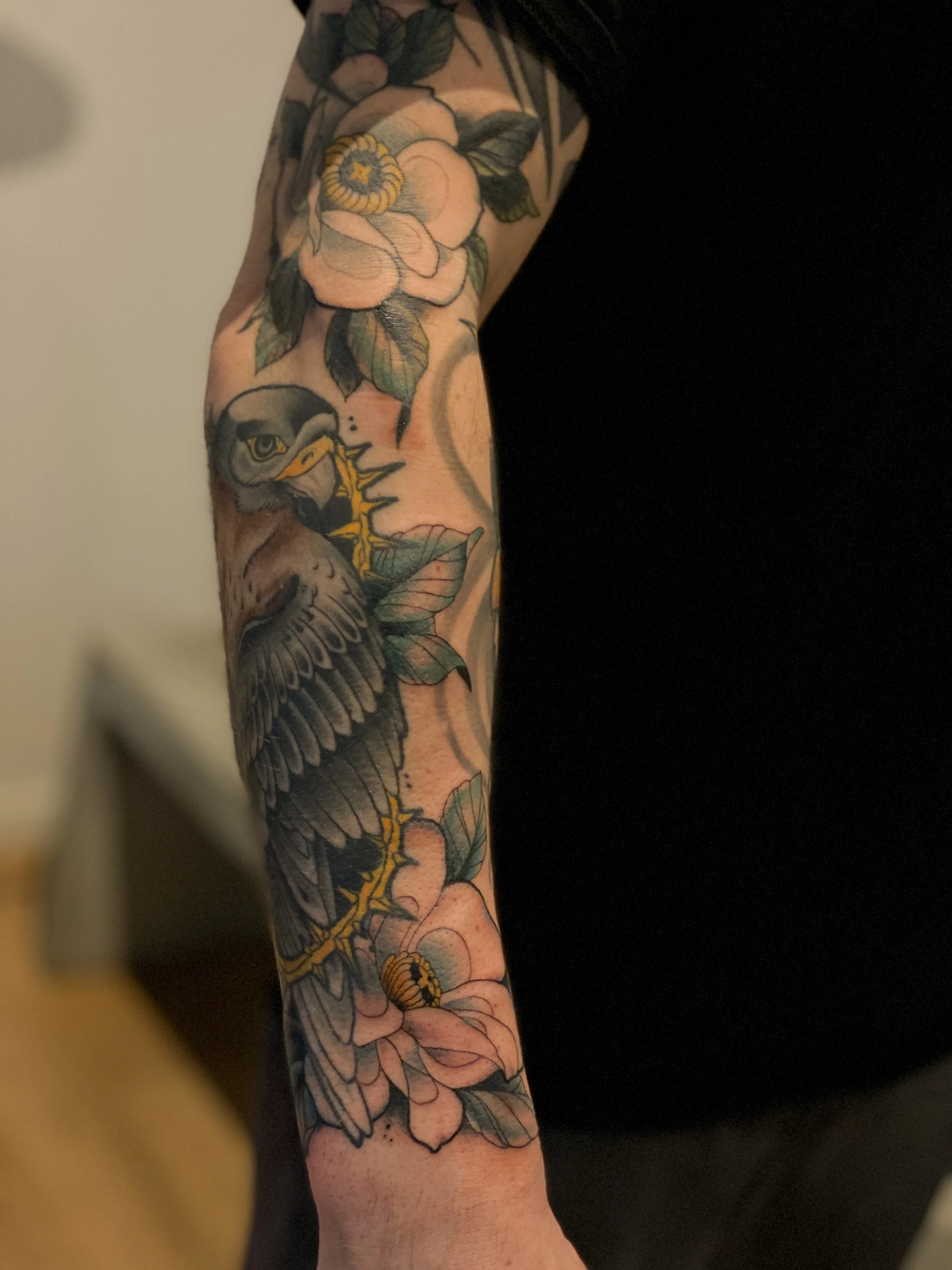 Tatovering af en ørn, der sidder på en blomst, omgivet af grønne blade, på en persons arm.