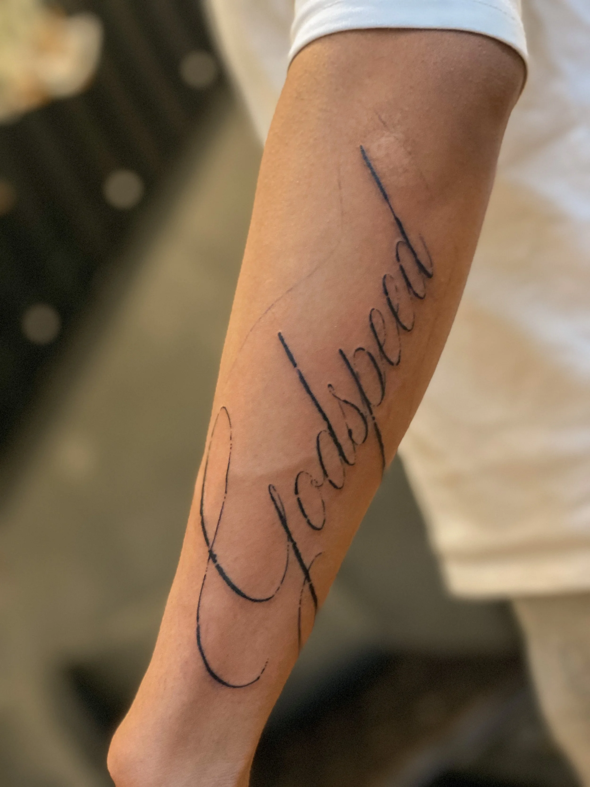 Tattoo med teksten "Cuidado de todas" i kursiv skrifttype på underarmen.