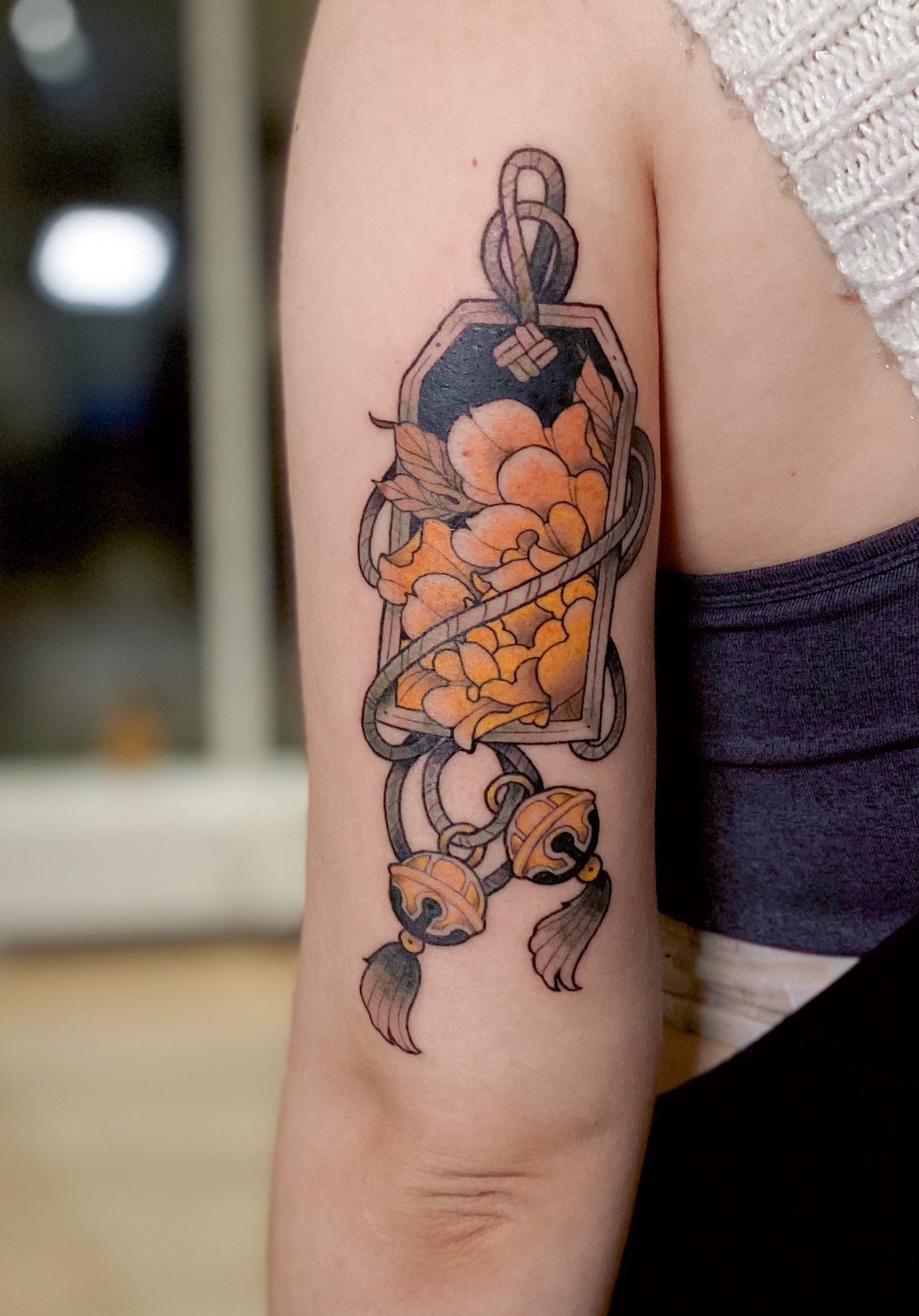 Tatovering af en nøgle med blomster og klokker på overarmen.