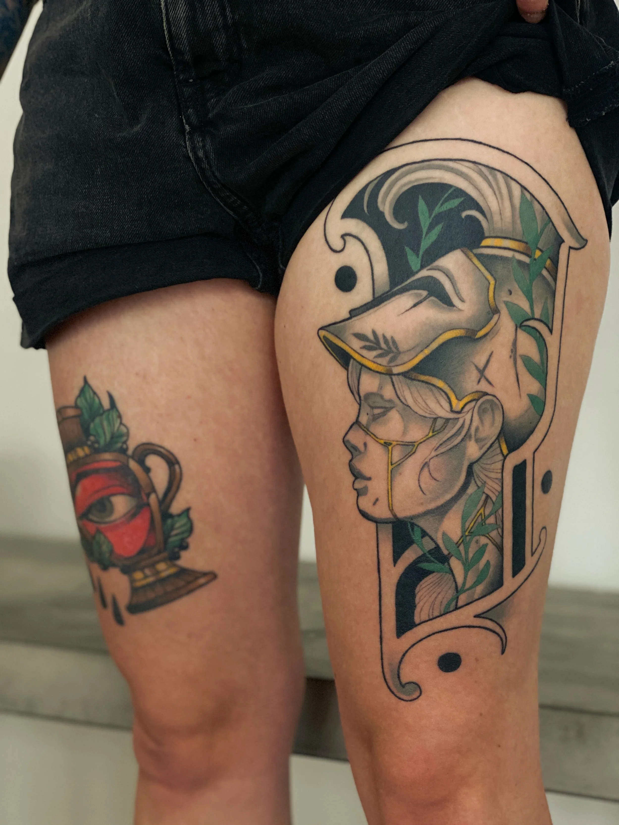 Tatovering af en kvindes ansigt i profil med et gammelt vaseskår, der dækker det meste af hendes hoved, omgivet af grønne blade og geometriske elementer.