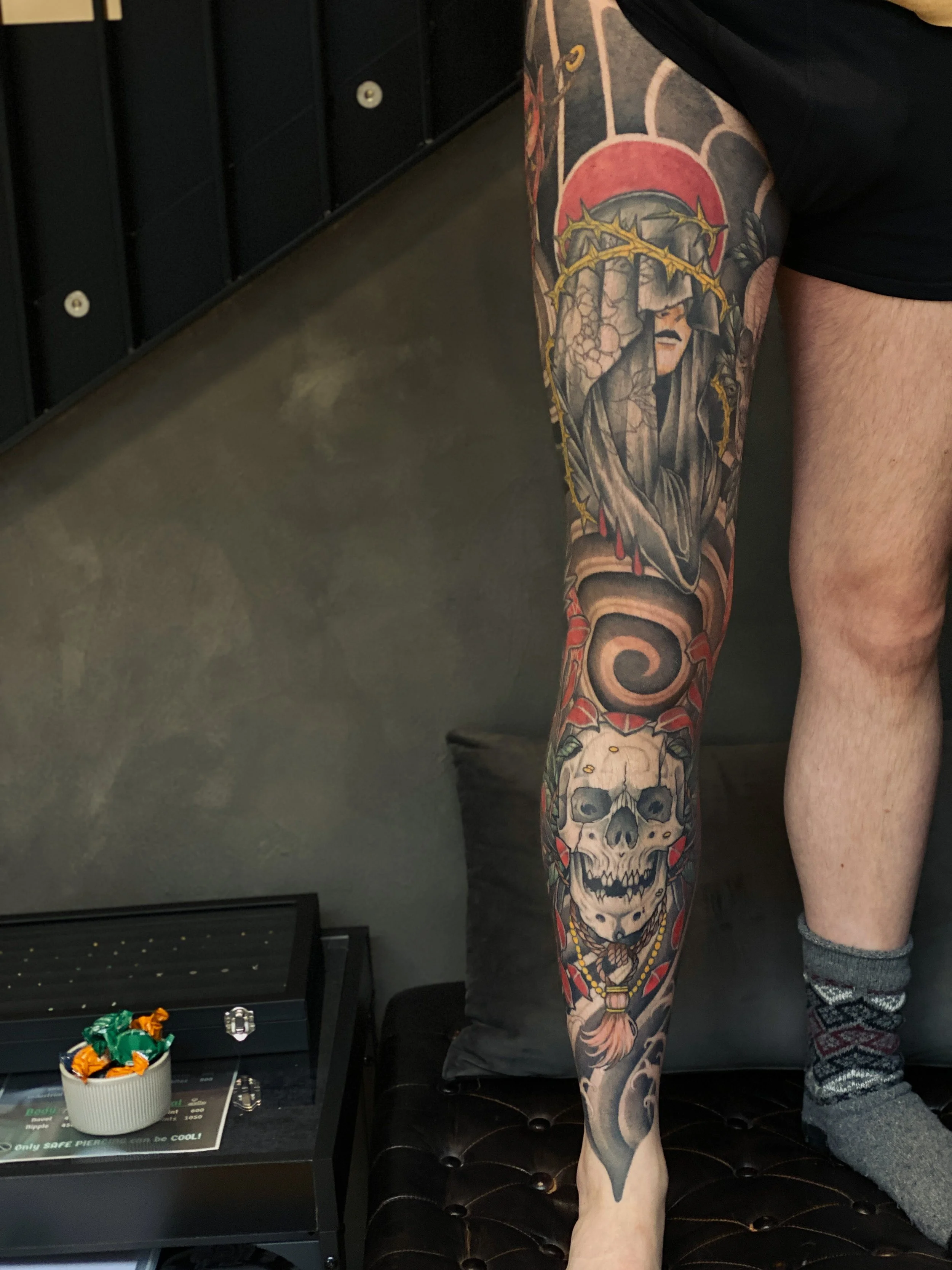 Person med ben tatoveret med en bibe, en dødningehoved og en rosenkrans.