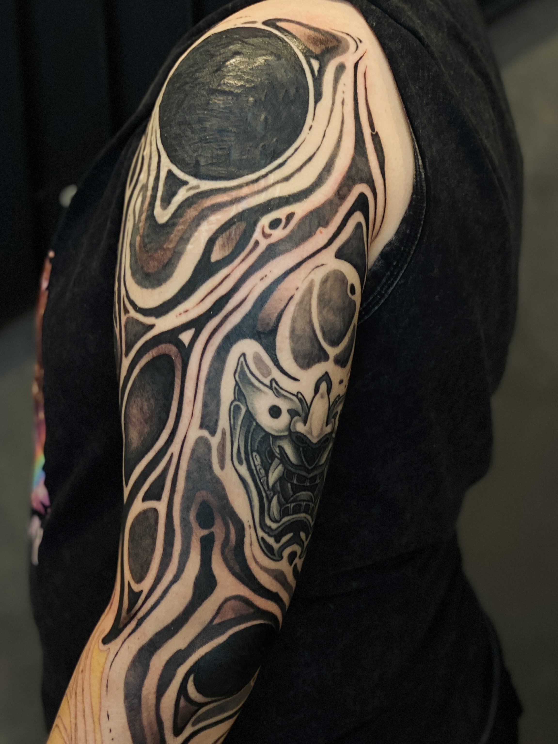 Tatovering på personens arm, der viser en drage og abstrakte mønstre i sort og grå nuancer.