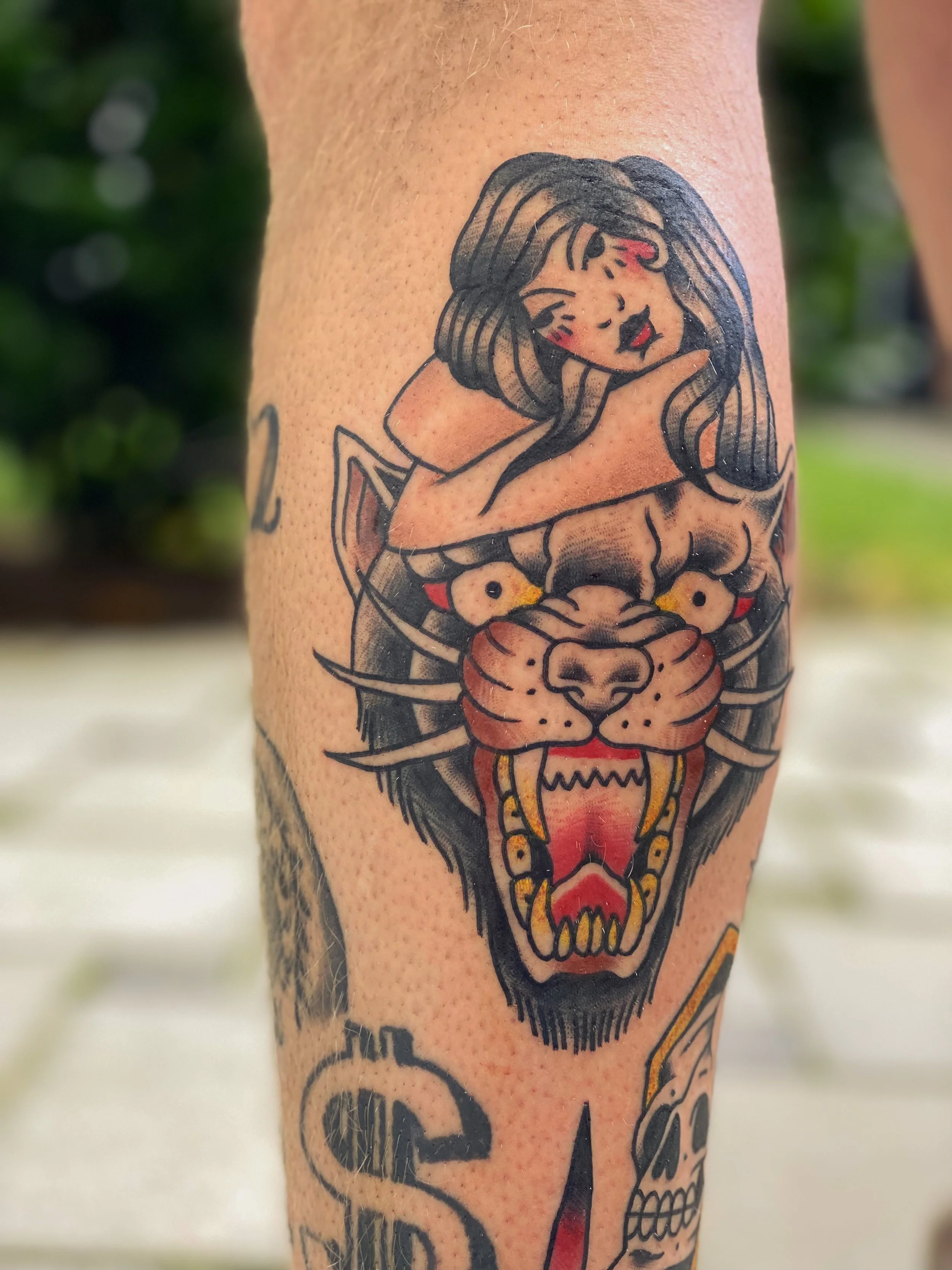 Tatovering af en kvindelig figur med mørke hår, sammen med en stor tigerhoved med åbent munde og skarpe tænder.