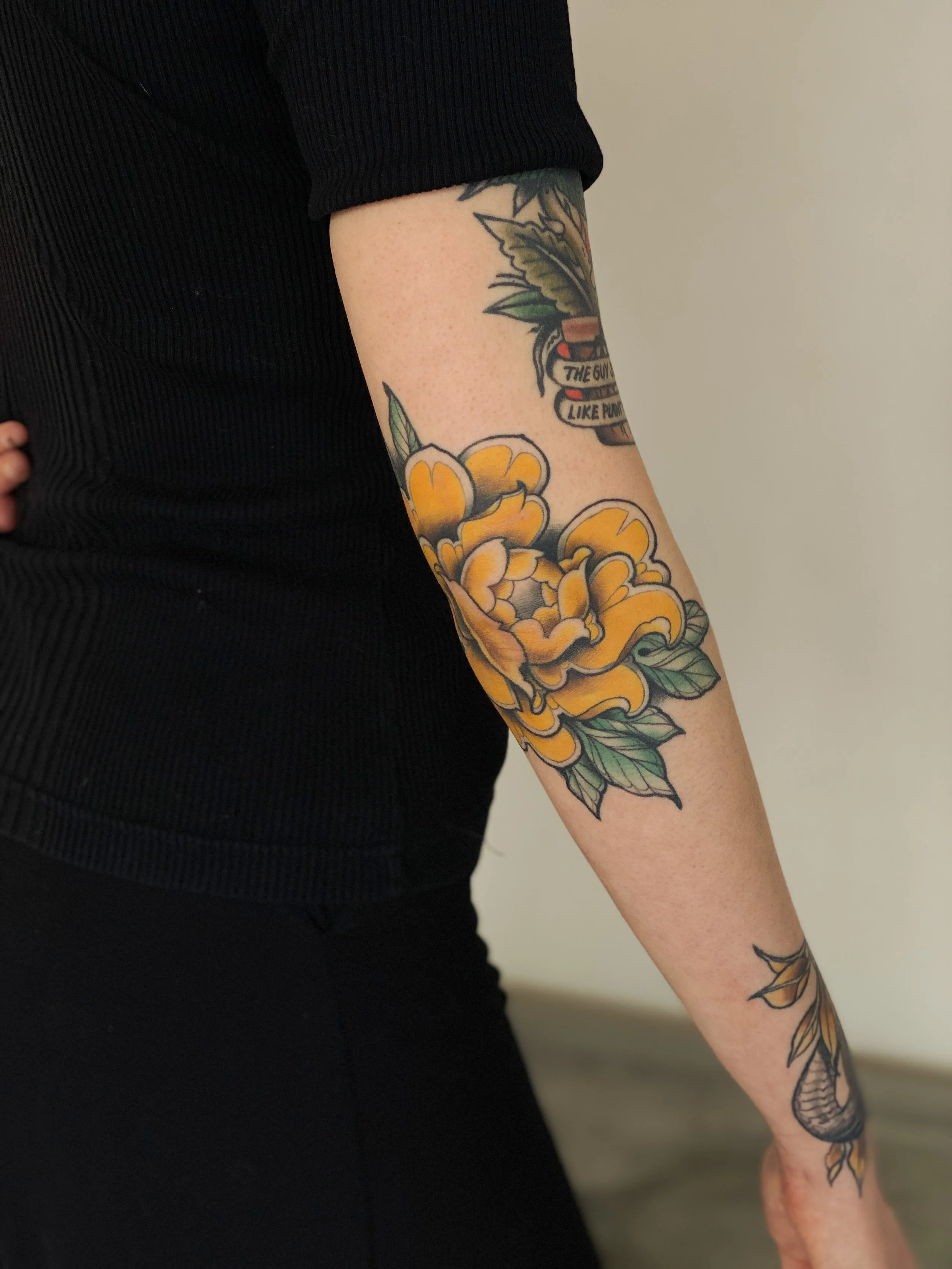 Tatovering af en stor gul og orange blomst på underarmen.