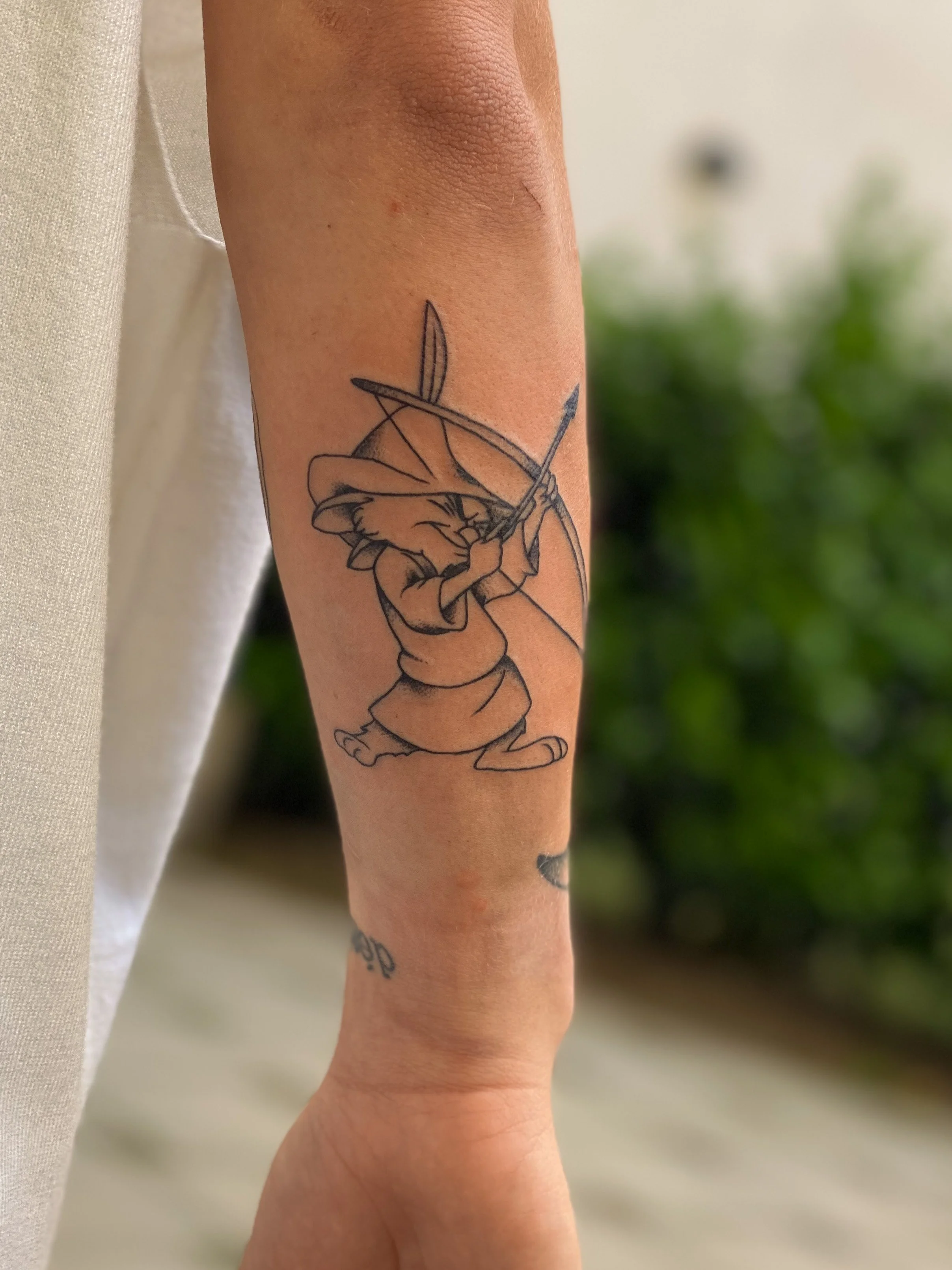 Tatovering af en tegneserie-løve, der skyder med bue og pil på underarmen.