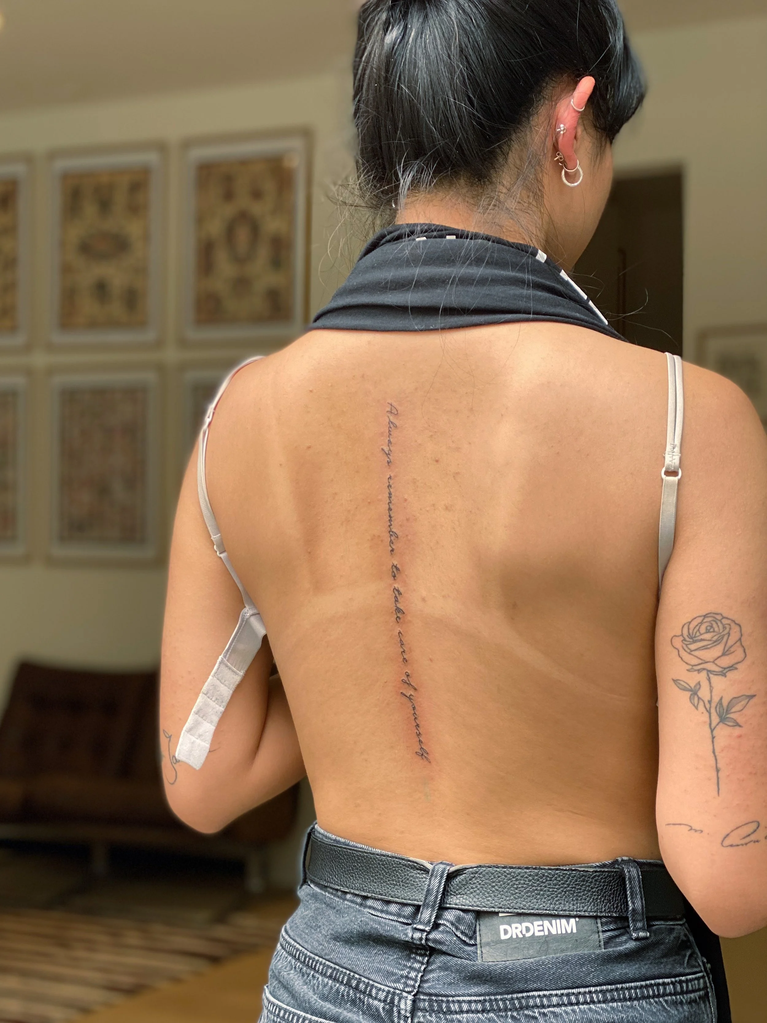 En kvindes rygvisning med en lang, kursiv tekst-tatovering. Tatoveringen siger, 'Always emerge as a better version of yourself.'