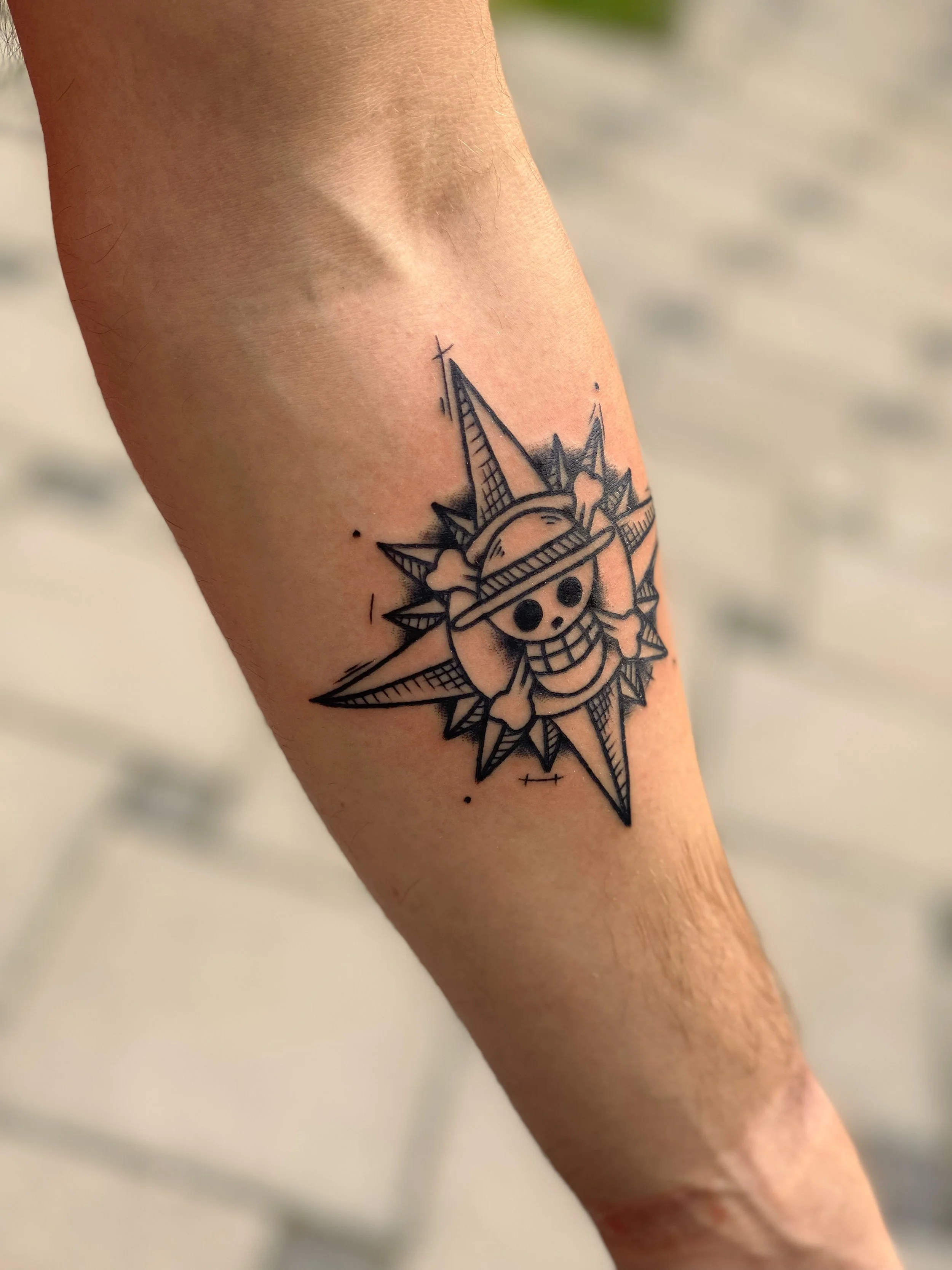 Tatovering af en figur med et smilende ansigt, jakke, hat, med en baggrund af geometriske elementer og linjer.