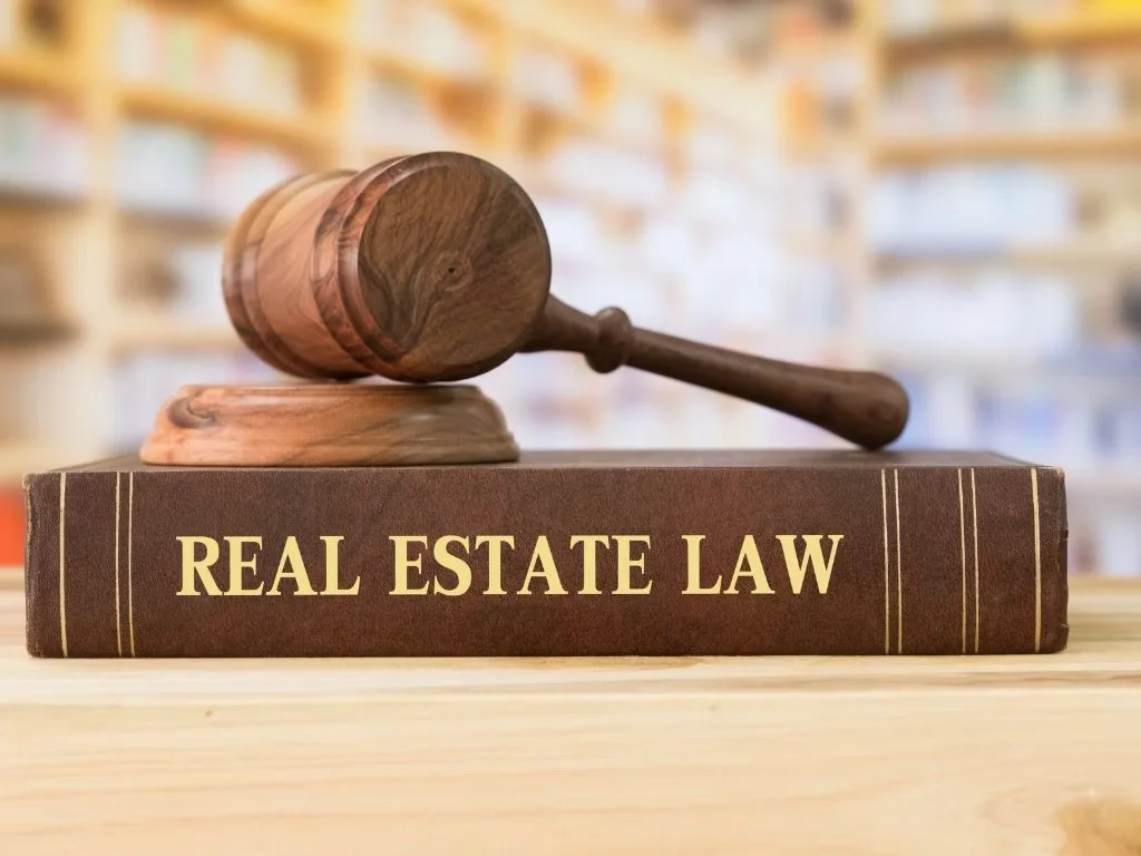 A gavel resting on a law book titled 'Real Estate Law' in a library or bookstore setting.