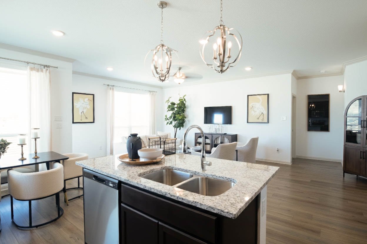 Professional real estate photography of a modern kitchen overlooking a large island, dining room, and open-concept front room. High-resolution shot featuring upscale pendant lighting and abundant natural light in a Central Texas home – Focus Point Me