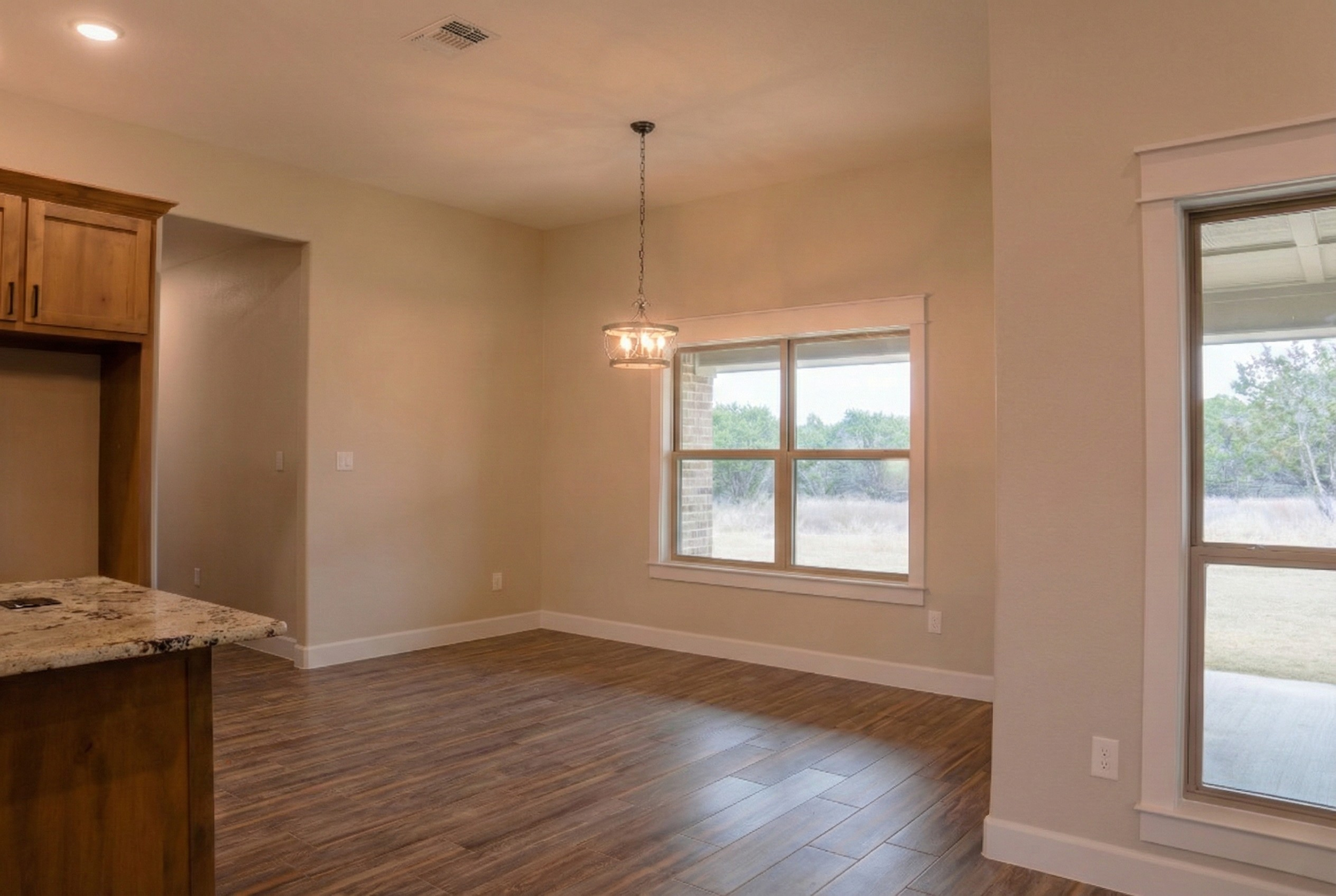 Professional real estate photography of a sunlit breakfast nook in a 3,500 sq ft luxury home. View features large windows with natural light, a modern pendant light fixture, and a partial view of the kitchen island. Serving Austin, Round Rock, George