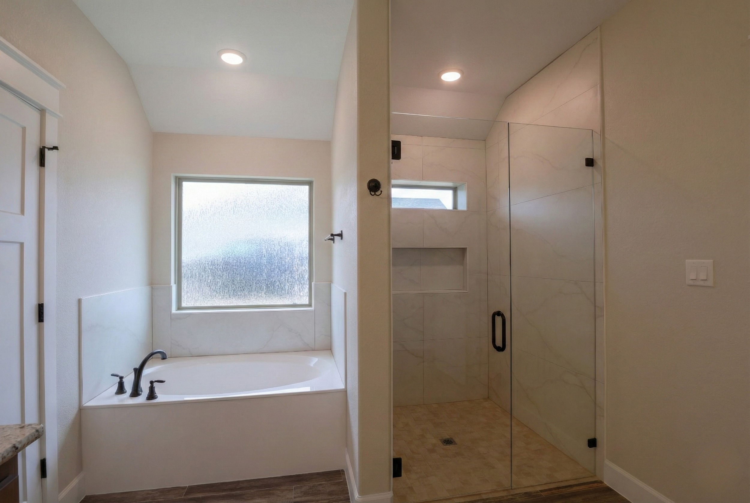 Professional real estate photography of a luxury master bathroom featuring a soaker tub under a large frosted glass window and a walk-in shower with floor-to-ceiling tile. High-resolution interior shot for Central Texas listings in Austin, Round Rock