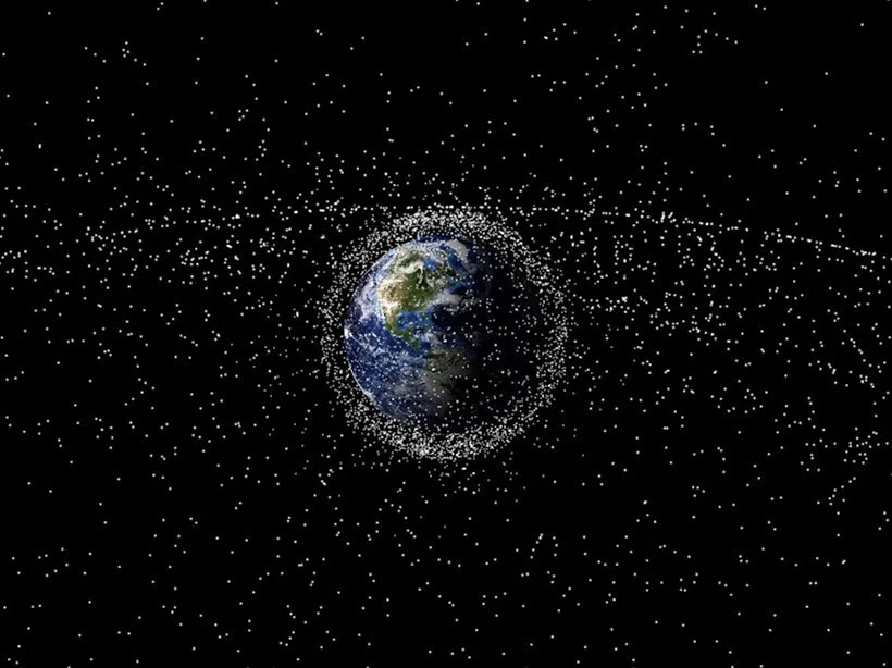 Earth surrounded by a belt of space debris or satellites, with numerous small white particles scattered throughout the black background of space.