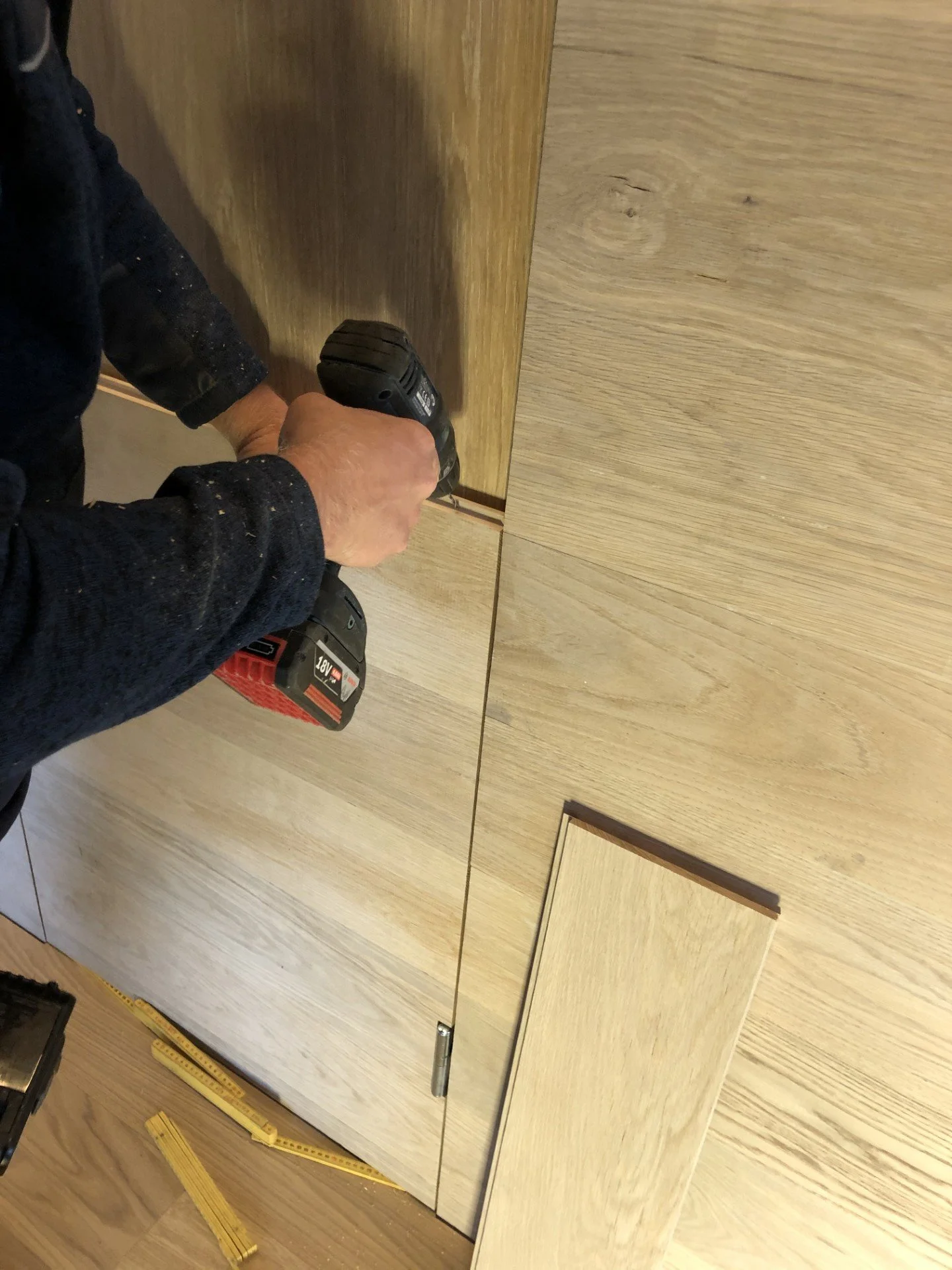 Person som bruker en elektrisk skrutrekker til å montere en treplate på en vegg eller skap.