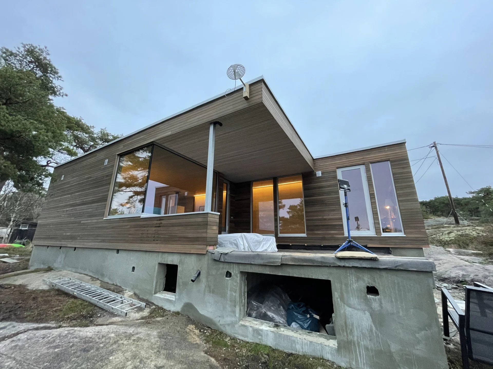 Nytt hus under konstruksjon med trepanel og store vinduer, bygget på en betongplate med åpent rom under.